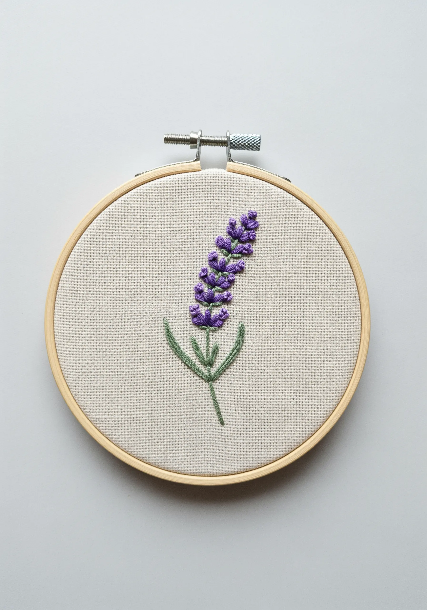 Close-up of embroidered lavender sprig with textured French knots in a wooden hoop.
