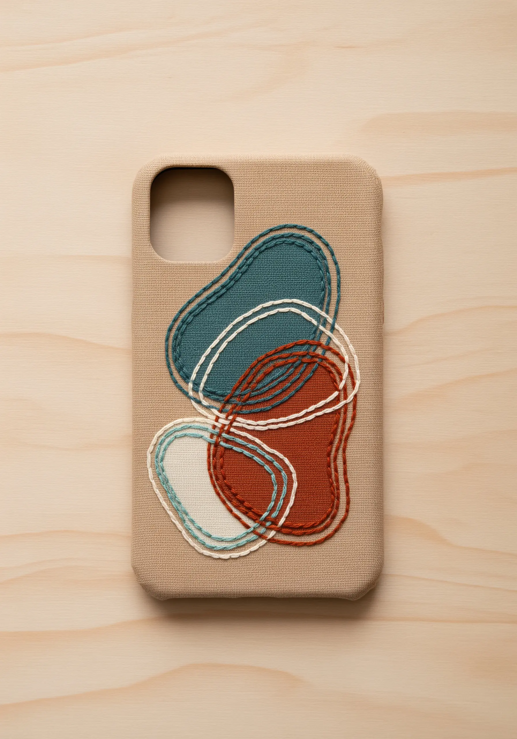 Abstract overlapping shapes in rust, teal, and cream embroidered on a beige phone case.