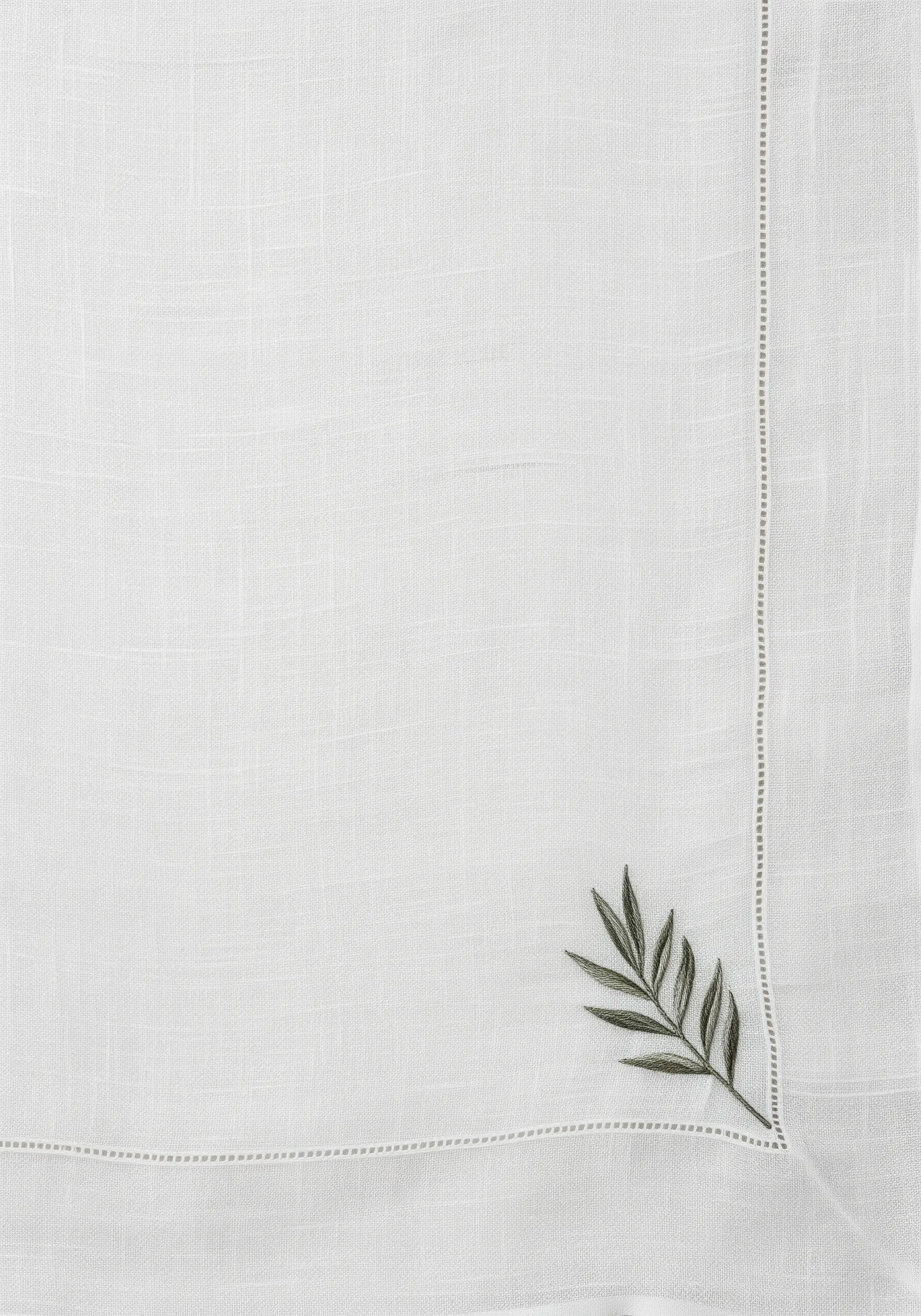 A single, minimalist olive sprig embroidered in the corner of a white linen napkin.
