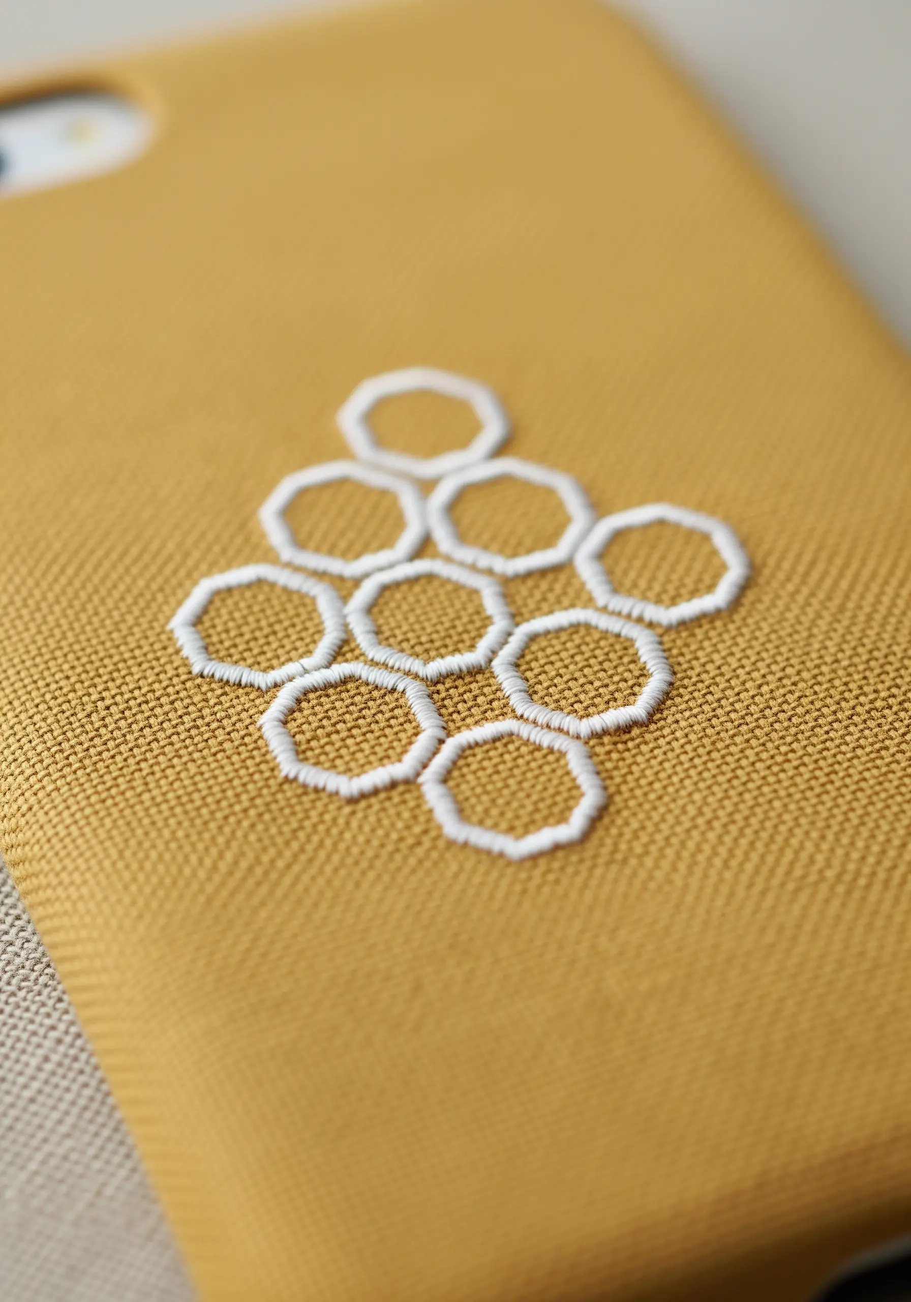 A geometric honeycomb pattern embroidered with white thread outlines on a mustard-yellow case.