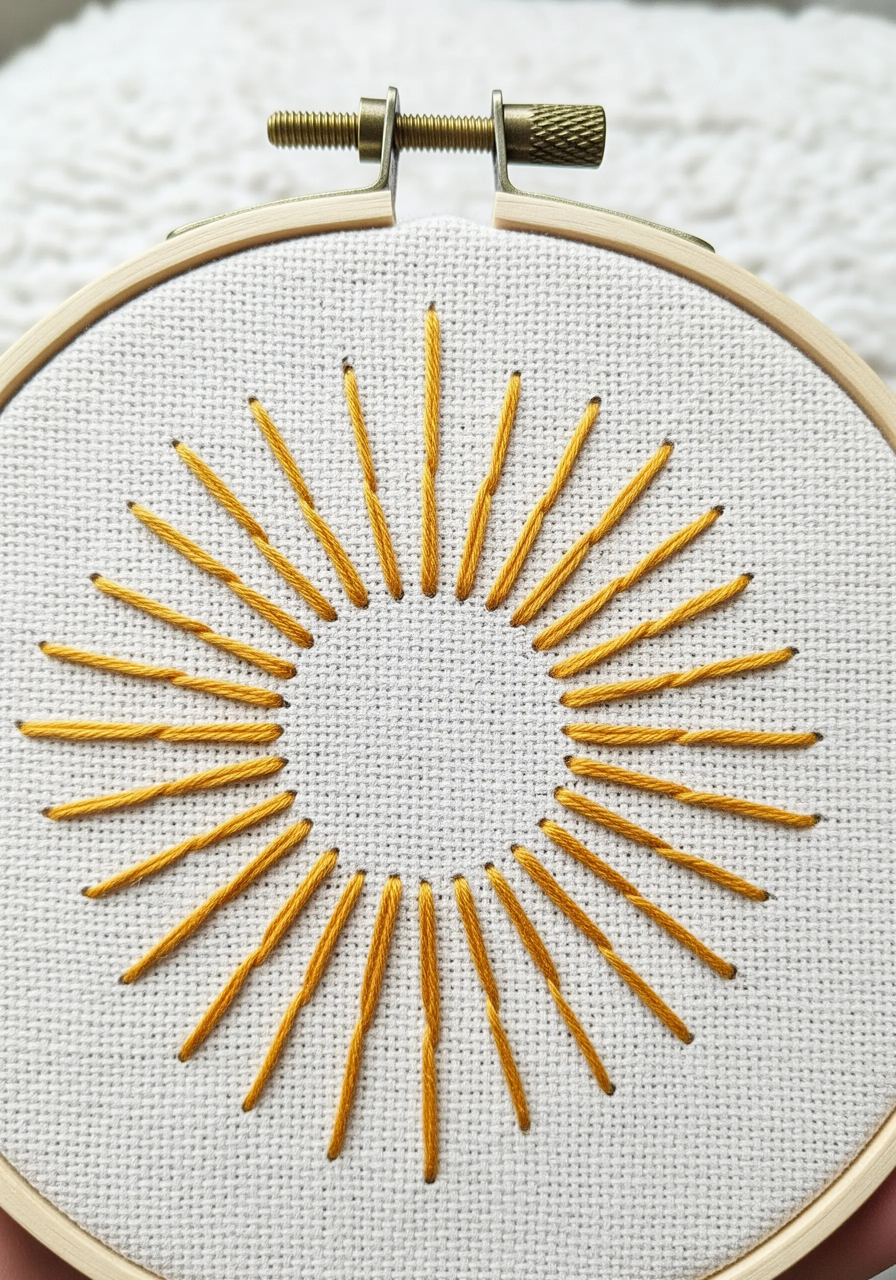 Minimalist sunburst embroidered with golden yellow thread in a wooden hoop.