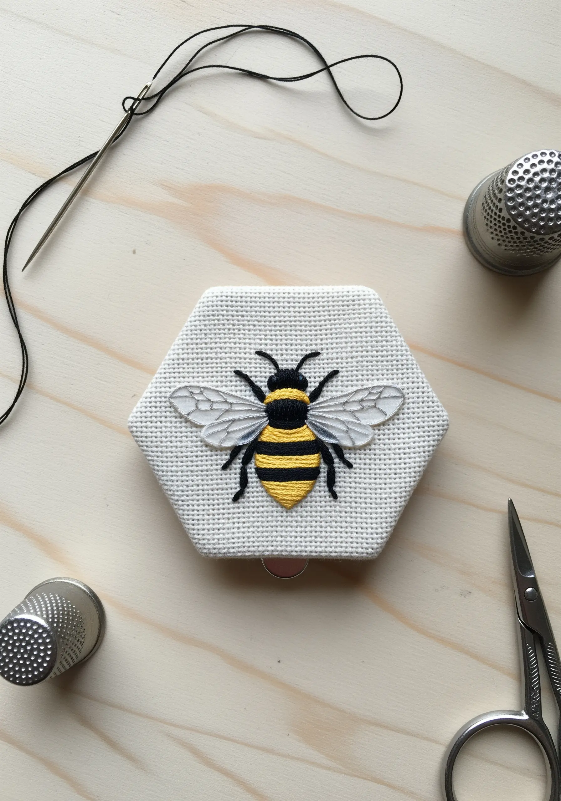 Embroidered bee with sheer organza wings, mounted on a hexagonal frame.
