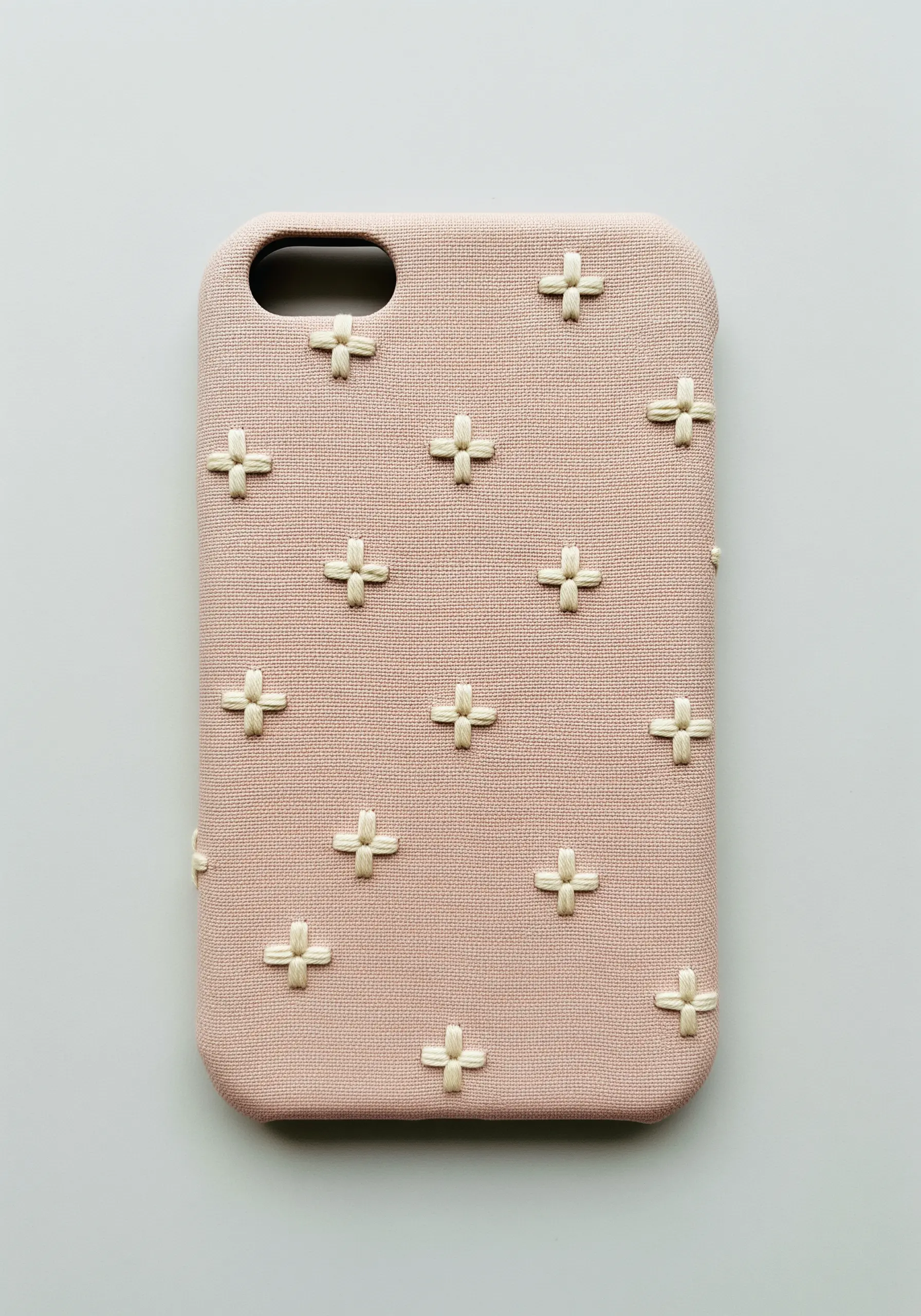 A repeating pattern of small embroidered plus signs in cream thread on a pink phone case.
