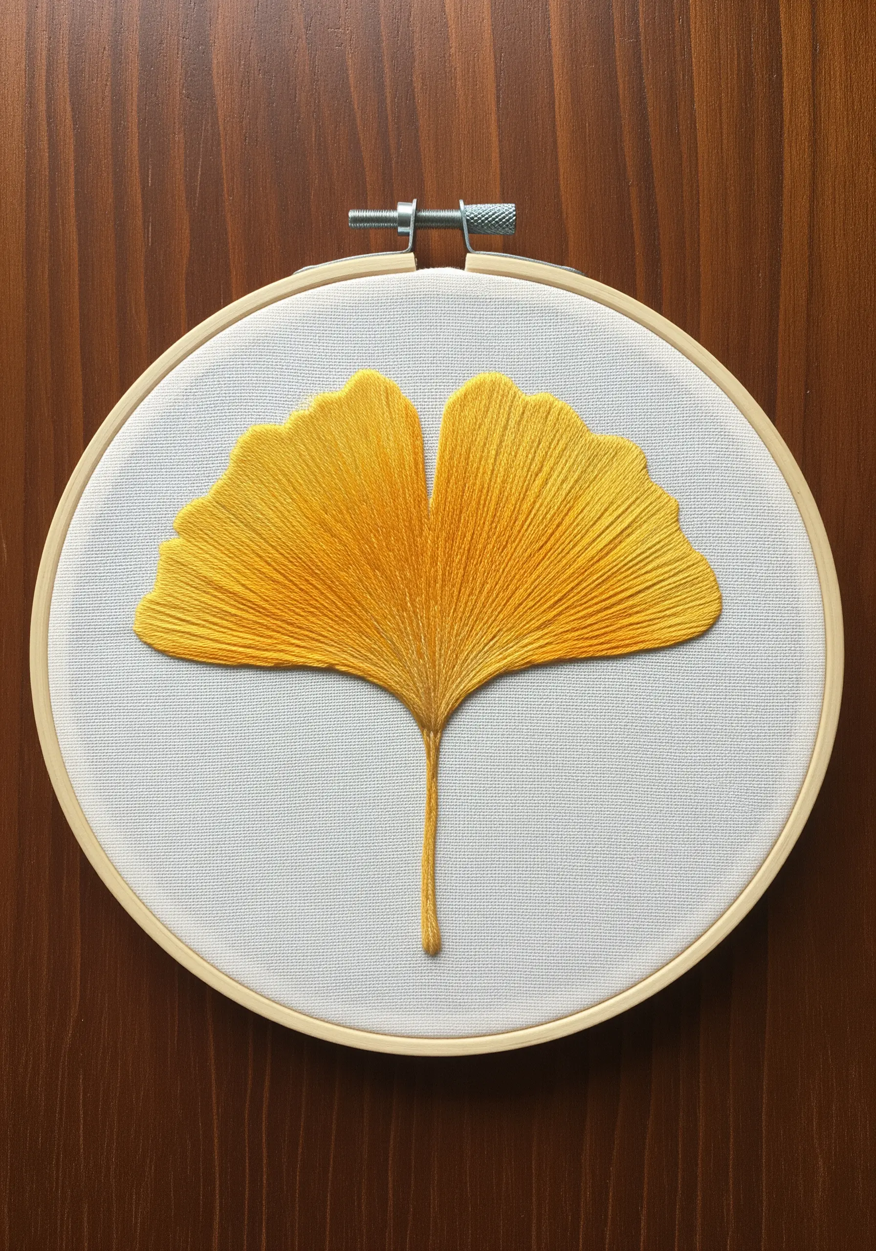 A simple, elegant embroidery of a golden yellow Ginkgo leaf on white fabric.