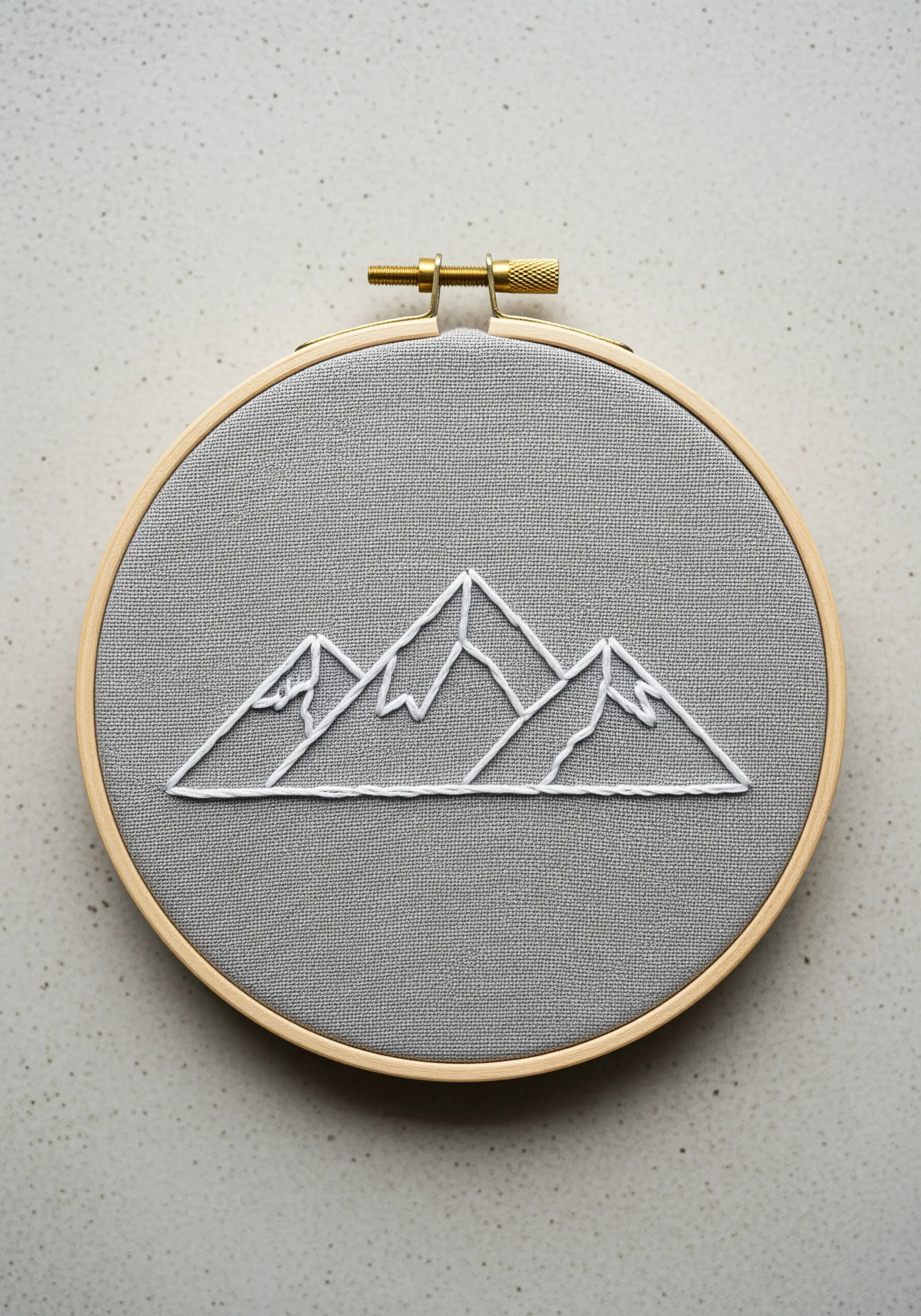 Minimalist mountain range outline embroidered in white thread on grey fabric.