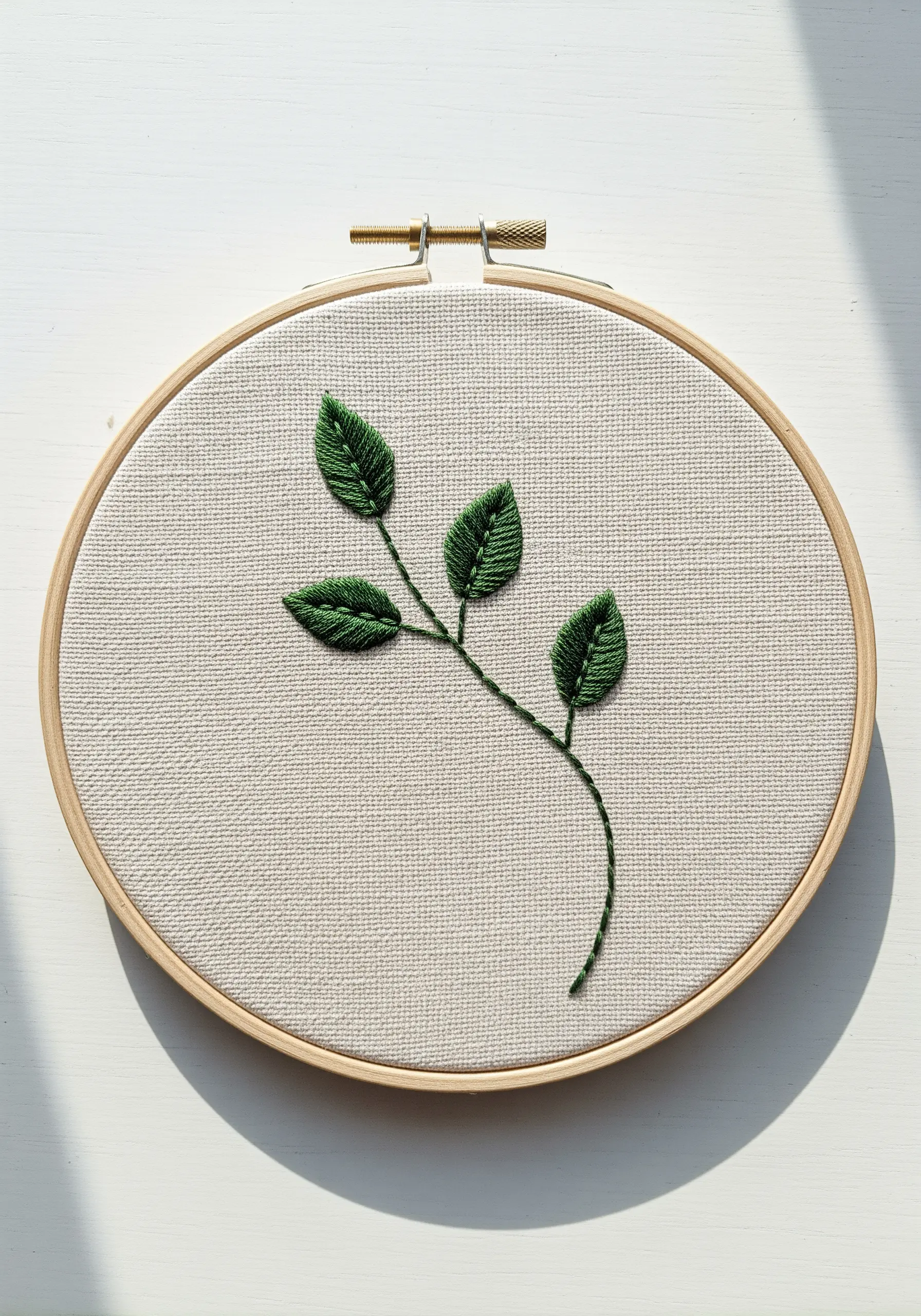 A simple sprig with three leaves embroidered in green fishbone stitch on white fabric.