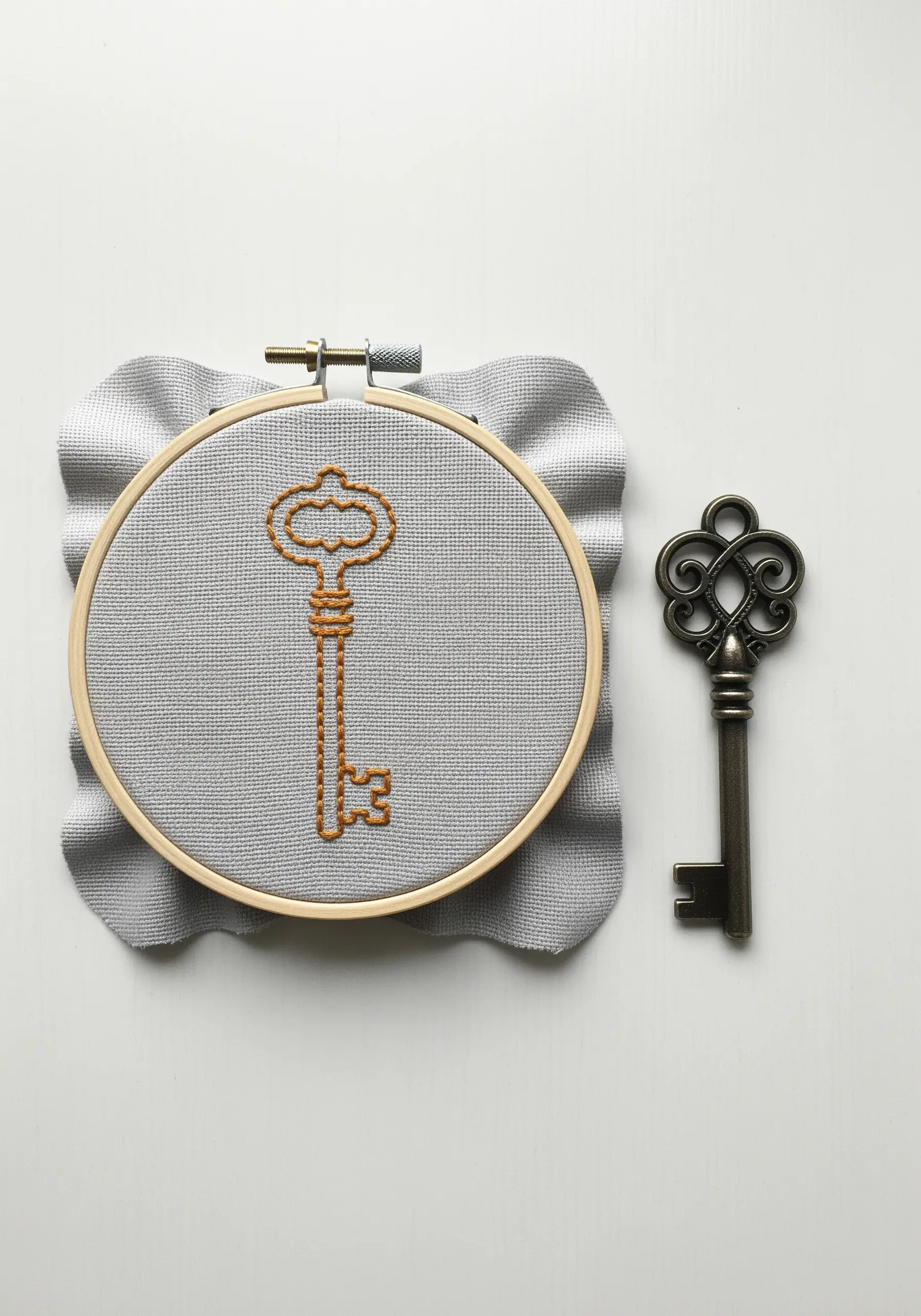 An ornate vintage key embroidered with a simple backstitch outline on grey fabric.