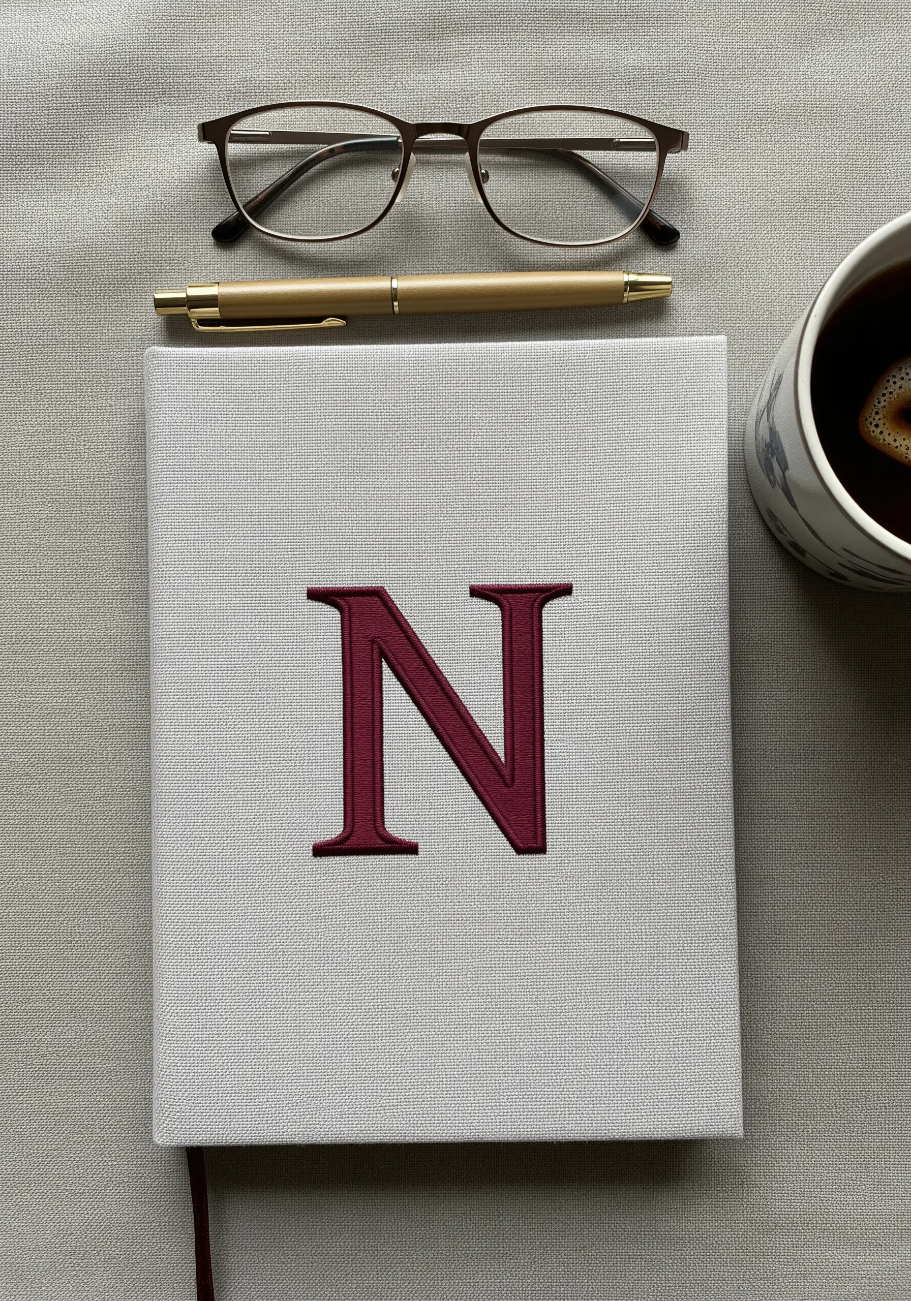 A classic serif letter 'N' embroidered in deep red satin stitch on a gray journal cover.