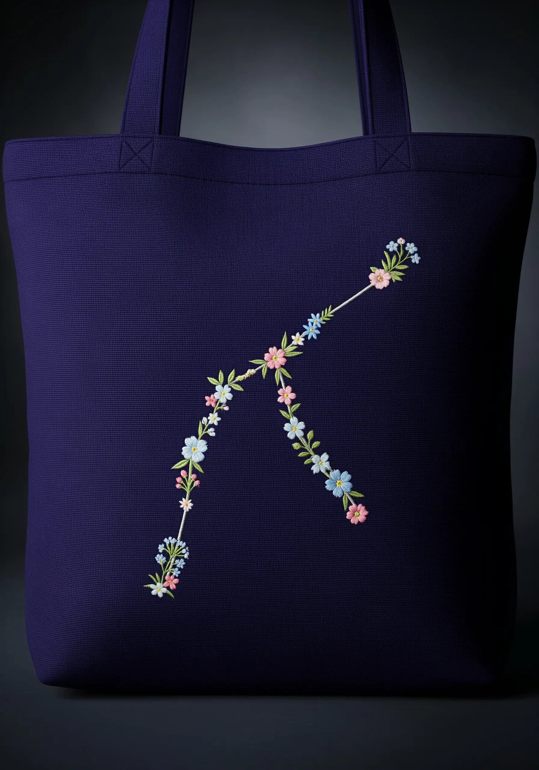 The letter K formed from tiny embroidered flowers and leaves on a navy tote.