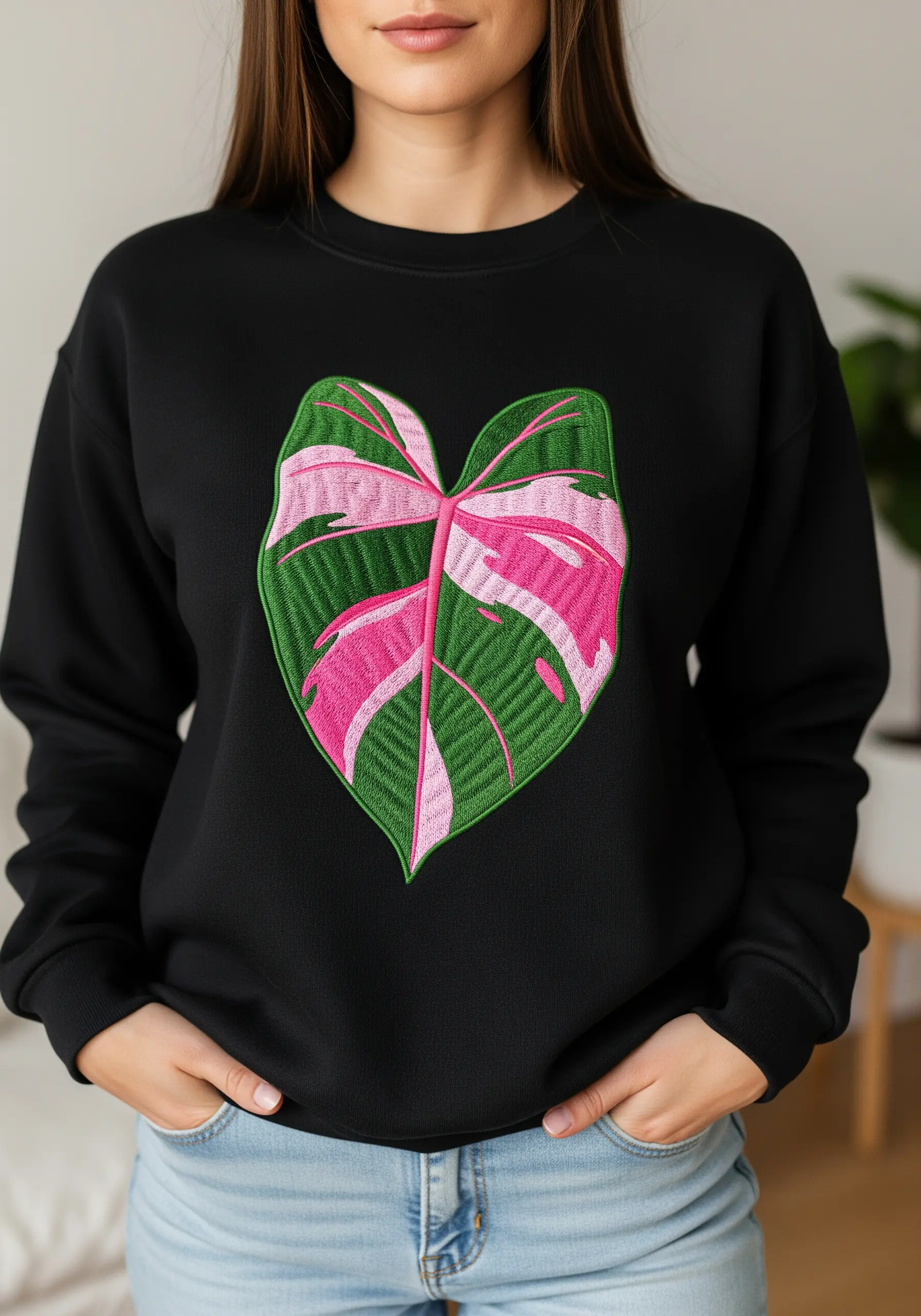 A woman wearing a black sweatshirt with a large Pink Princess Philodendron leaf embroidered on it.