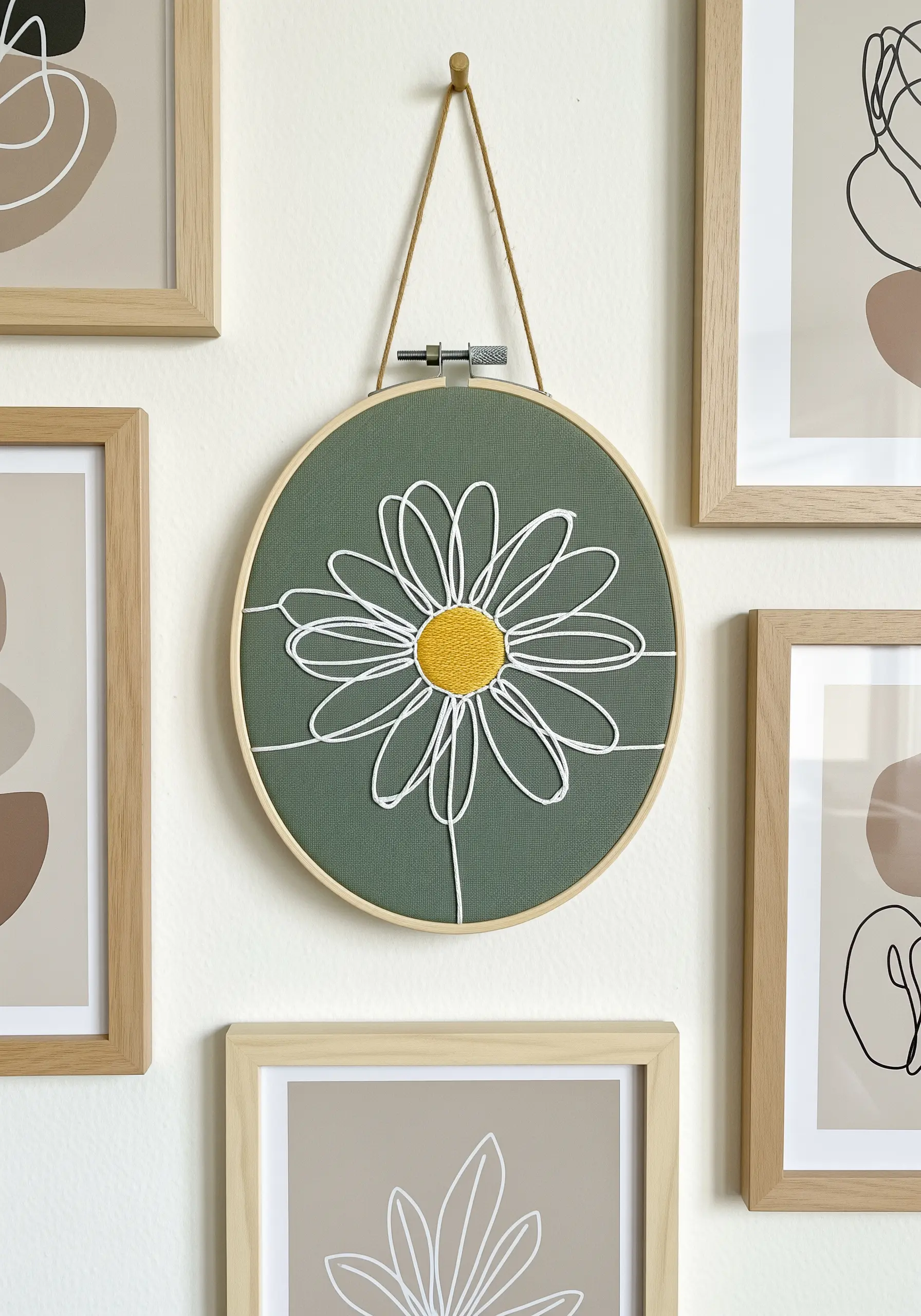 White line-art daisy with a yellow satin-stitched center on green fabric in a hoop.