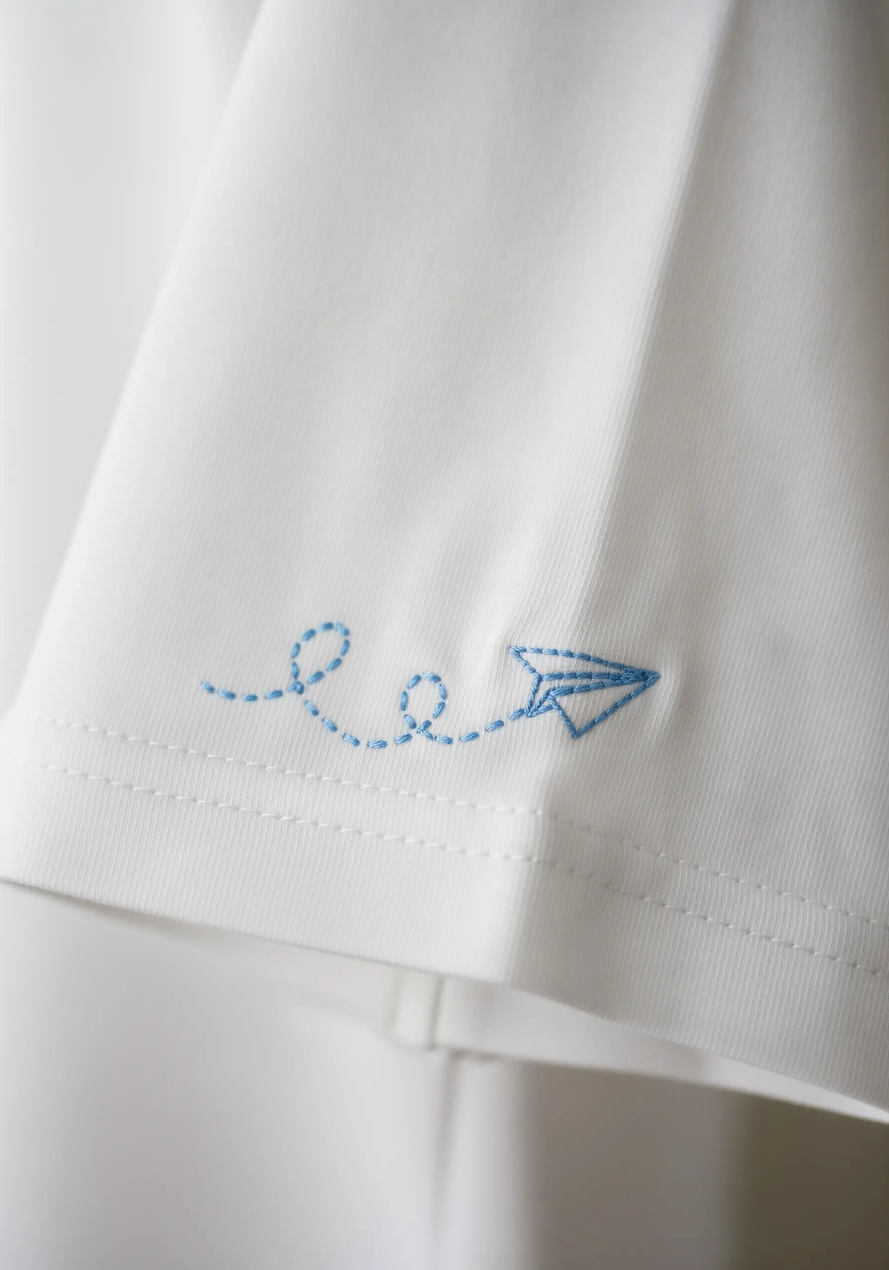 A blue paper plane with a dotted line trail embroidered on a t-shirt sleeve.