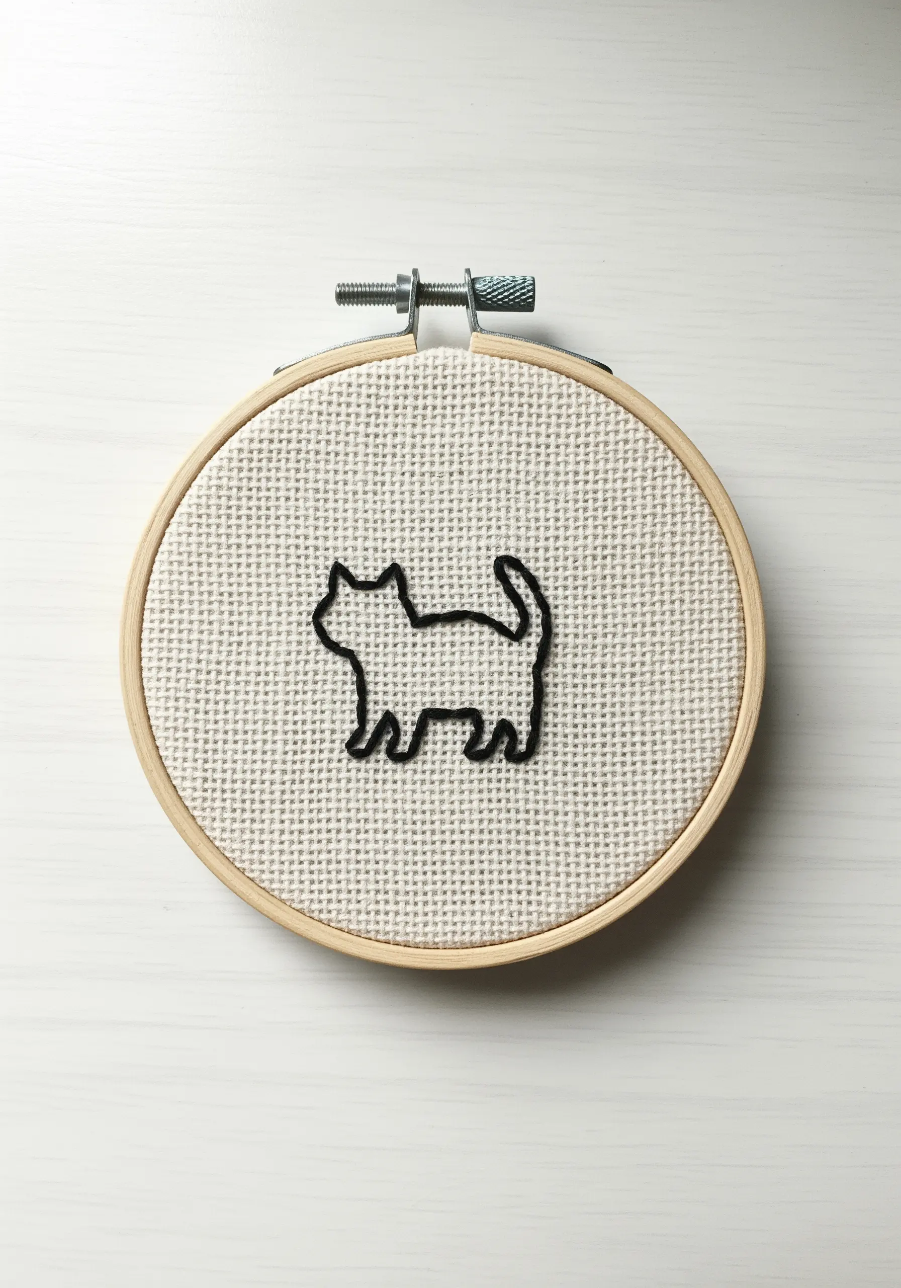 Minimalist black cat silhouette embroidered with a thick stem stitch on Aida cloth.