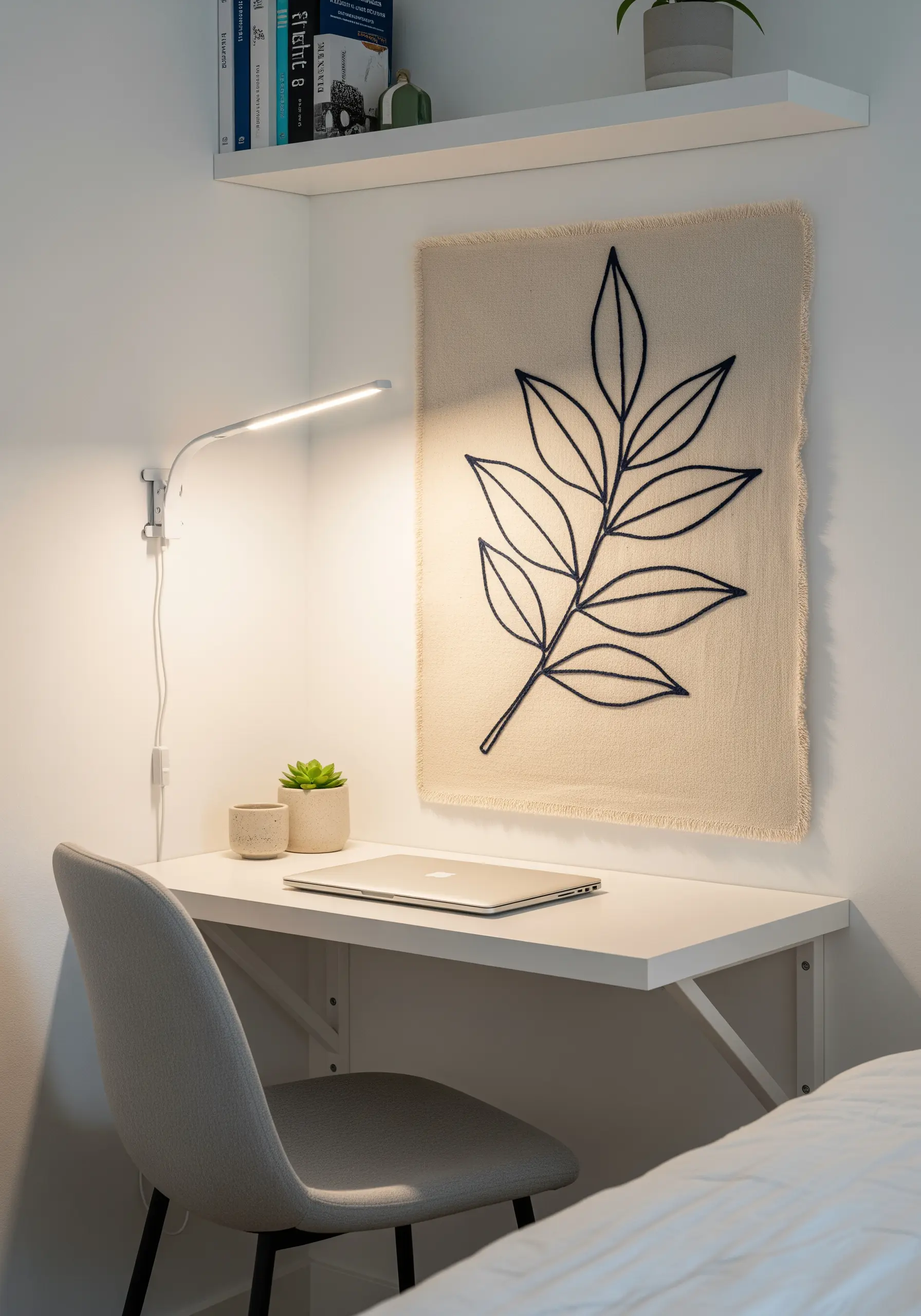 A bold, single-line leaf embroidery on a frayed-edge, natural canvas hanging above a desk.