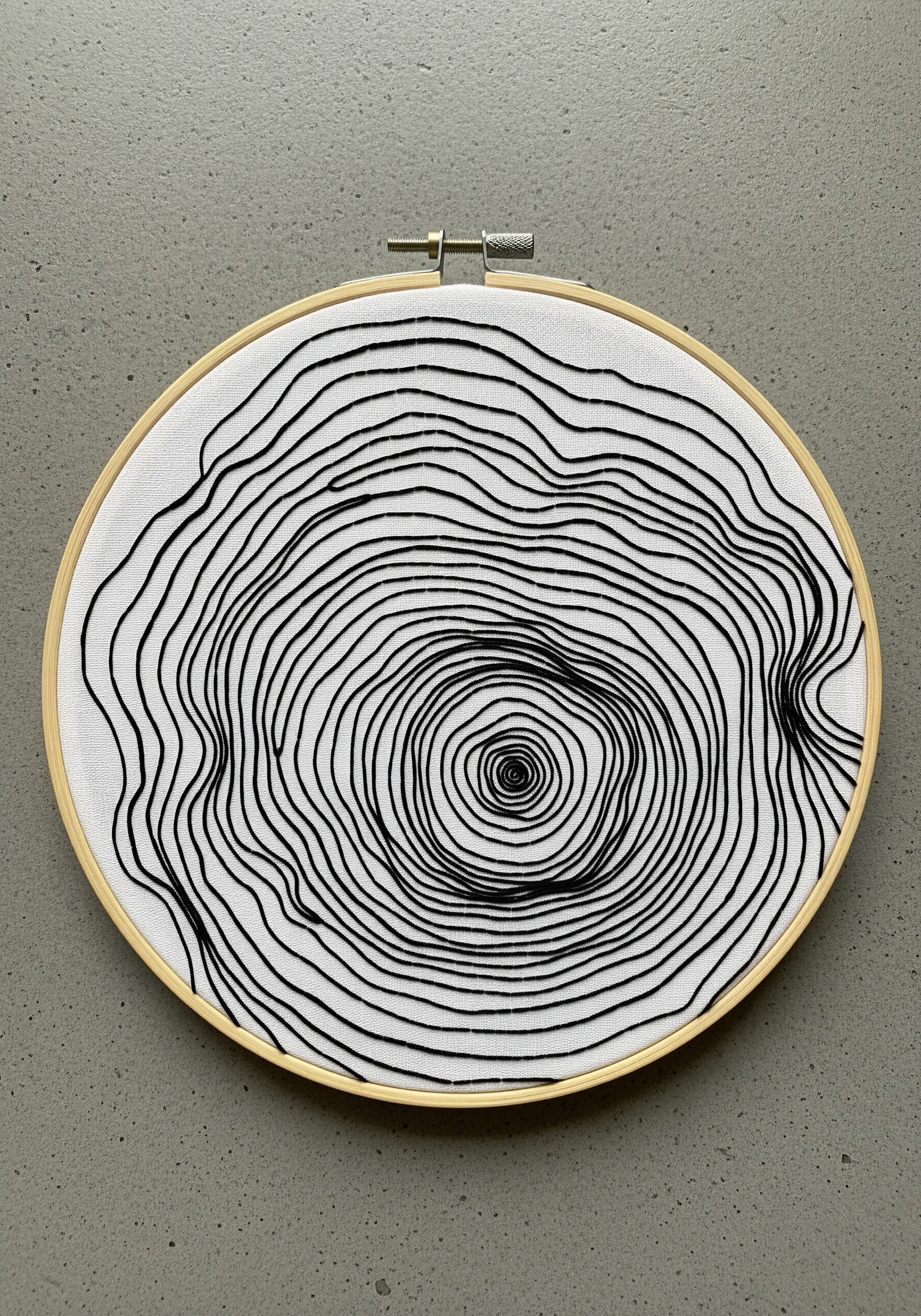 Minimalist black thread embroidery of organic, flowing tree ring lines on a white background.