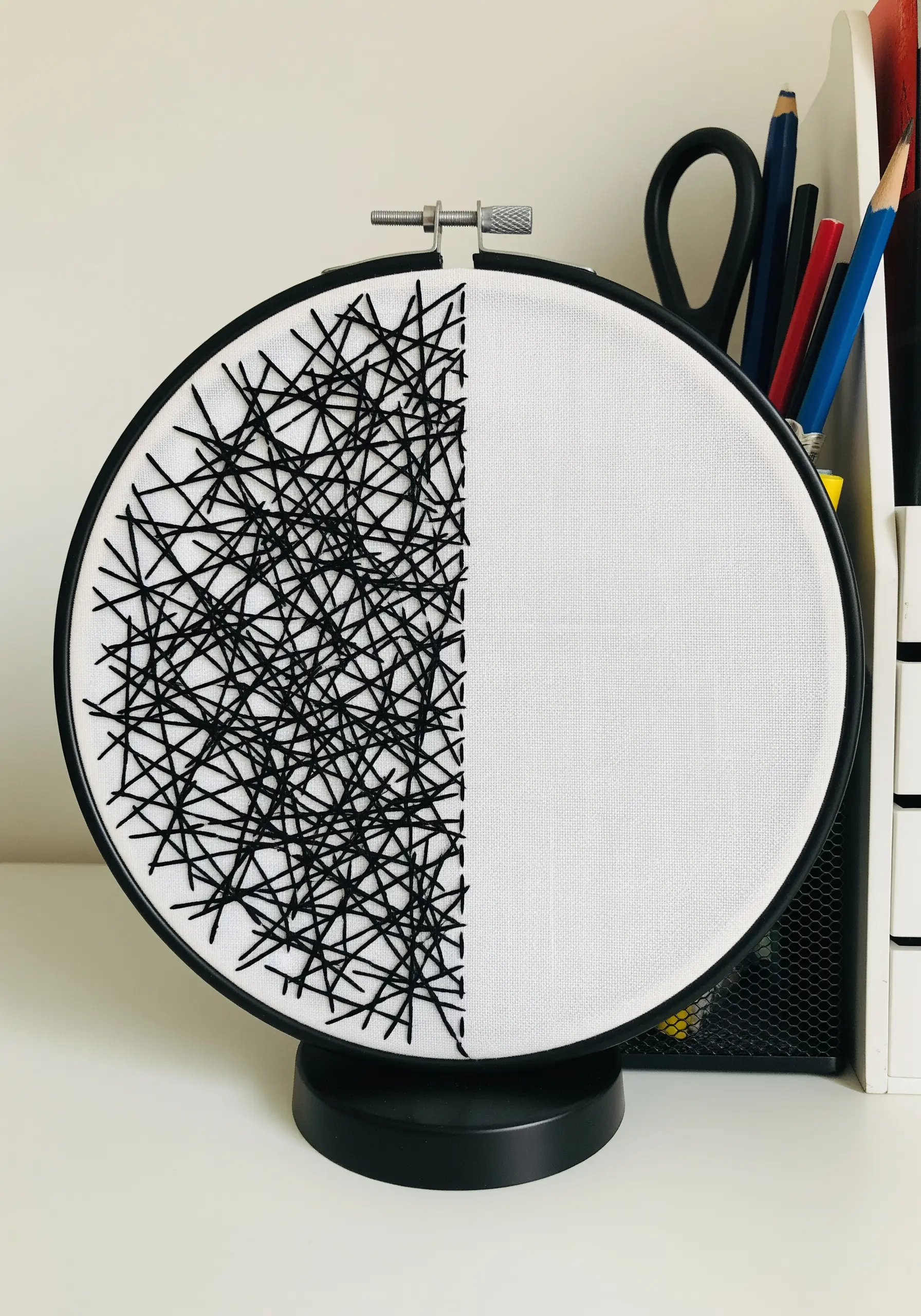 Half of the embroidery hoop is filled with chaotic black intersecting lines.