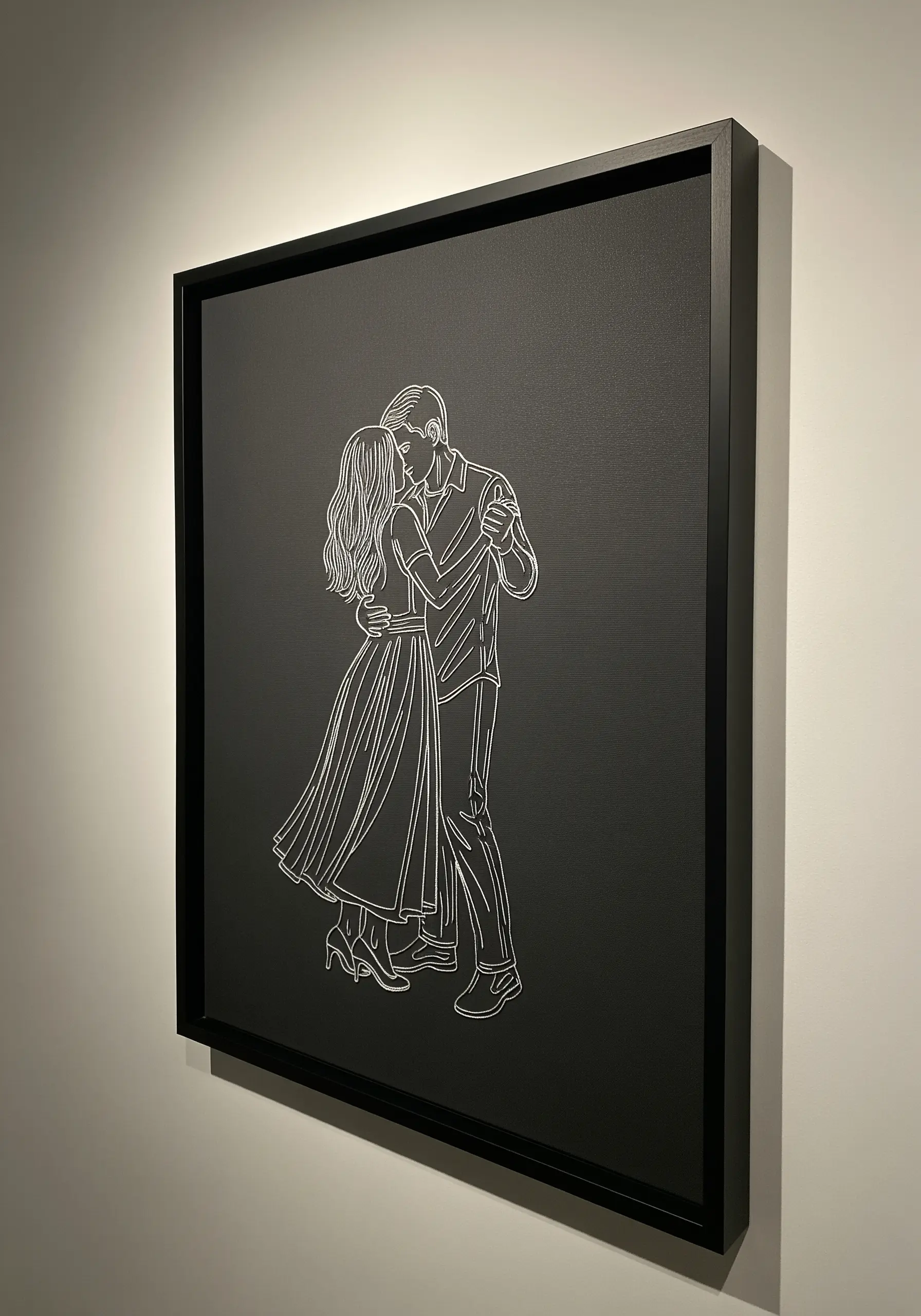 A line art portrait of a dancing couple, stitched in white on black canvas and set in a black frame.