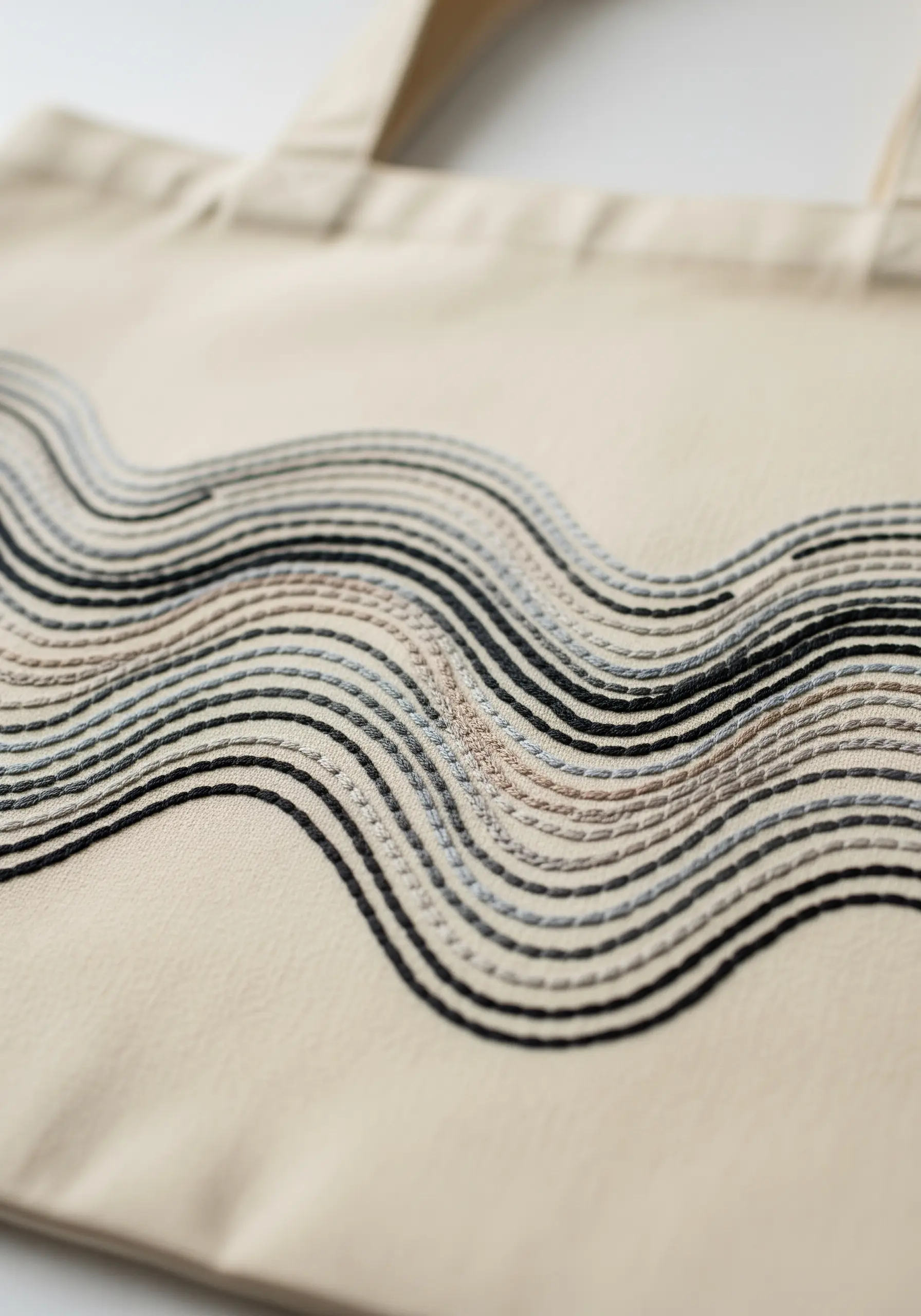 A close-up of wavy, parallel lines stitched in neutral tones on a canvas tote.