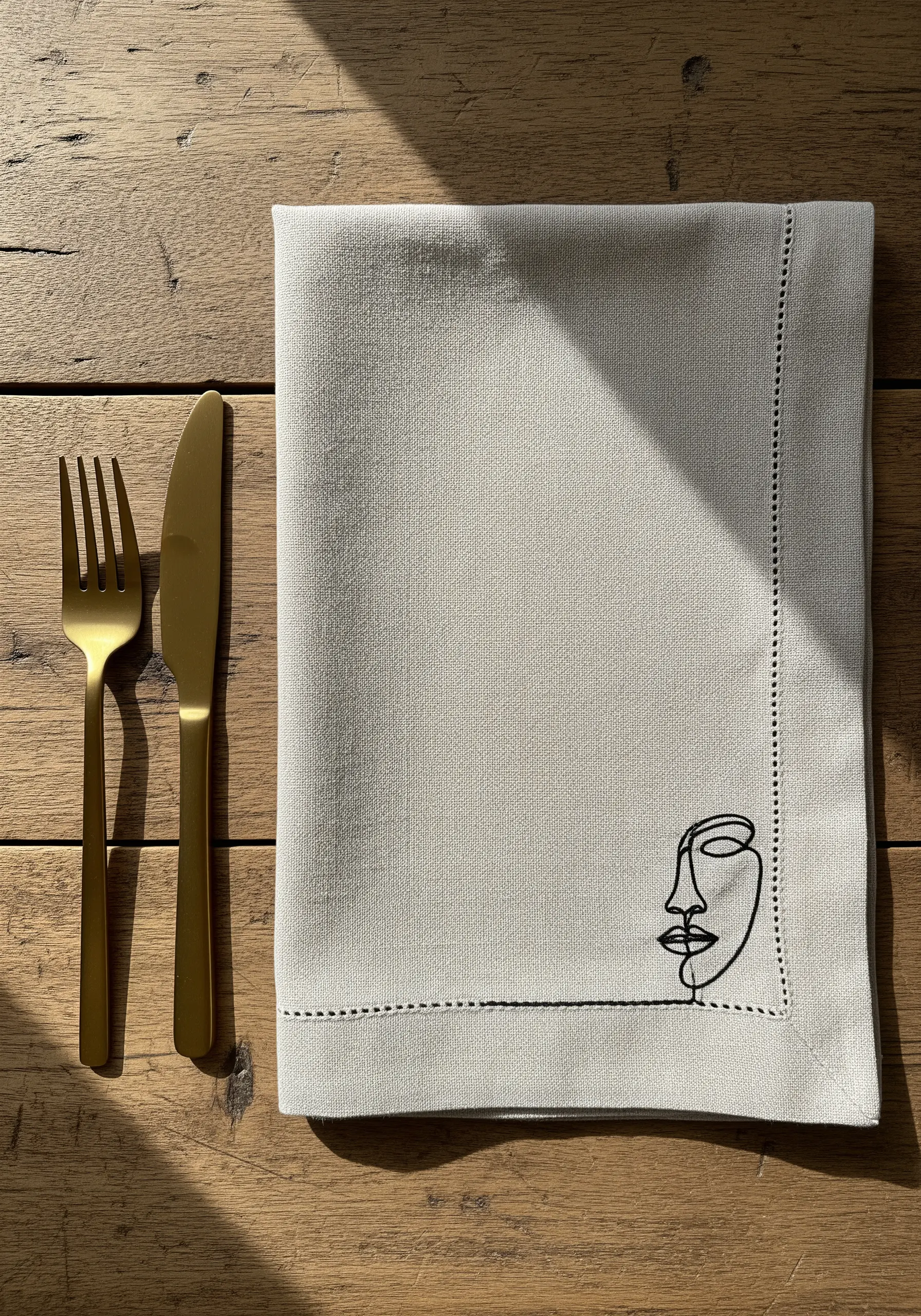 Minimalist one-line abstract face embroidered in black thread on a neutral linen napkin.