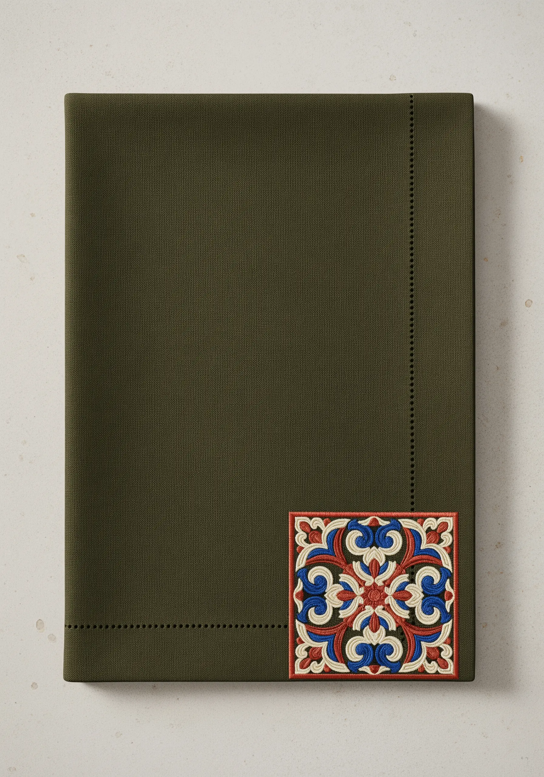 A single, ornate embroidered tile in red, blue, and white on a dark olive napkin.