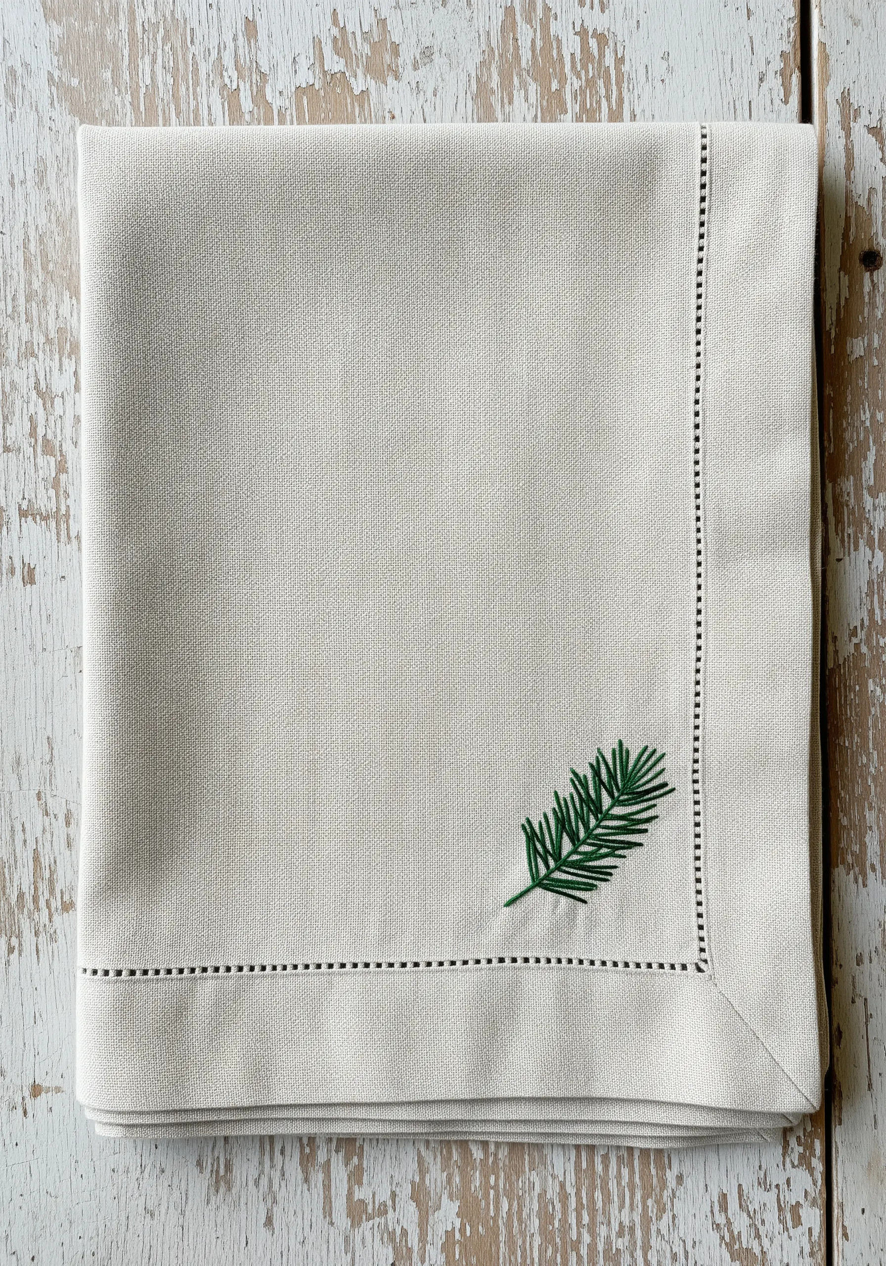 Minimalist pine sprig embroidered in dark green on a neutral linen napkin.