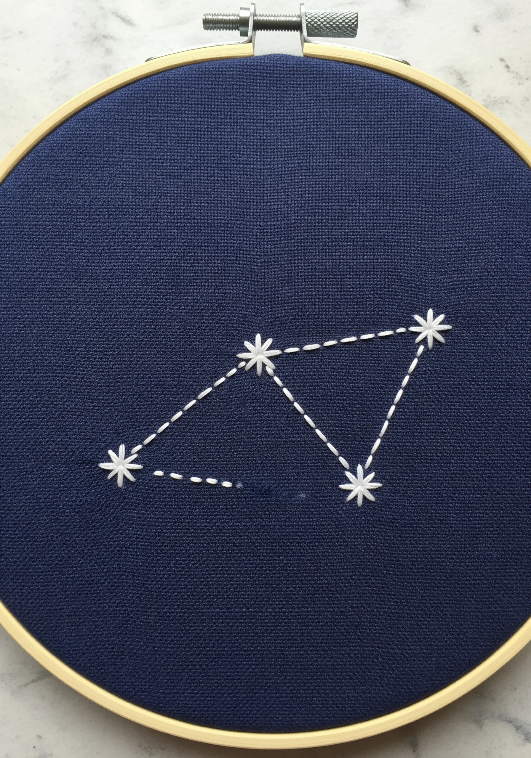 Embroidered constellation with star stitches and dashed lines on dark blue fabric.