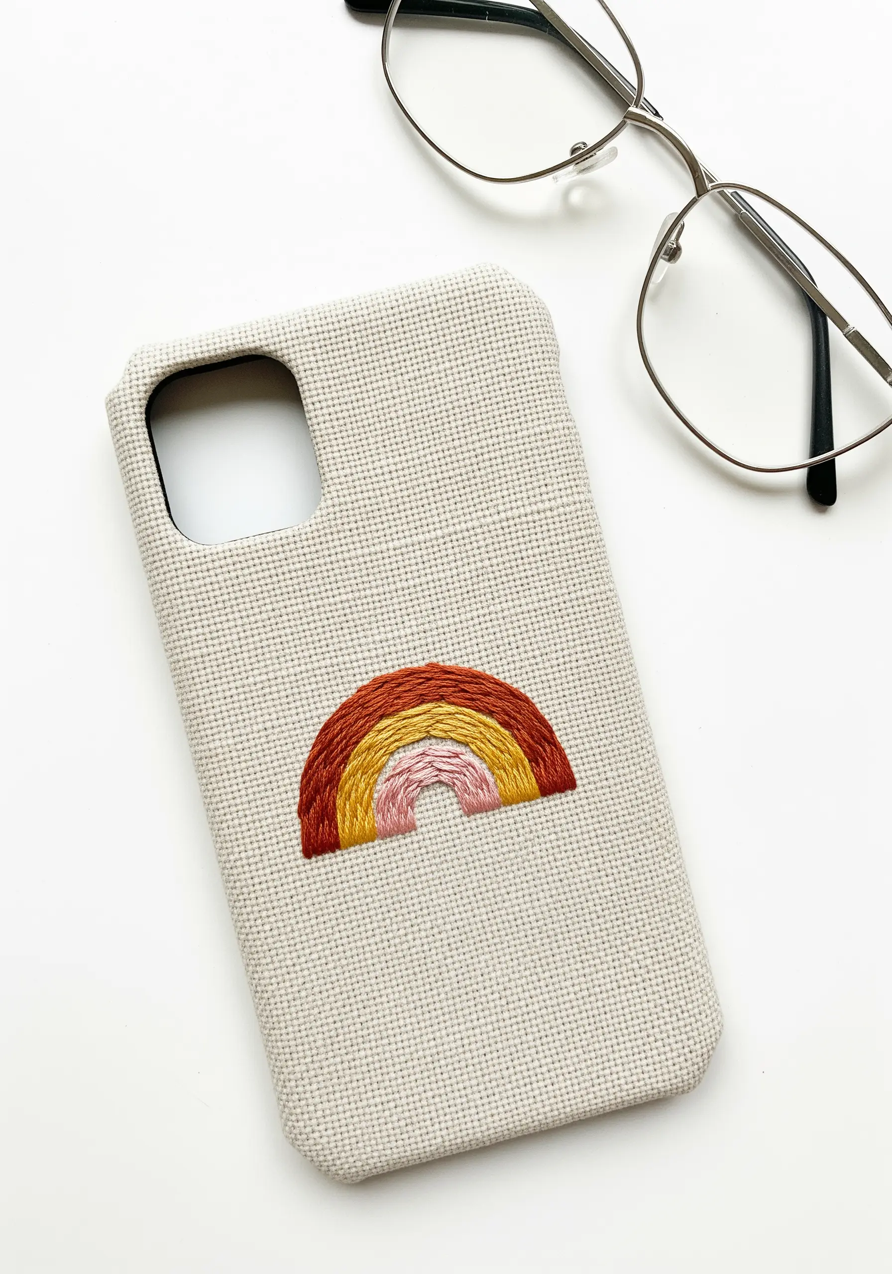 Close-up of a textured, earthy-toned rainbow embroidered on a phone case.