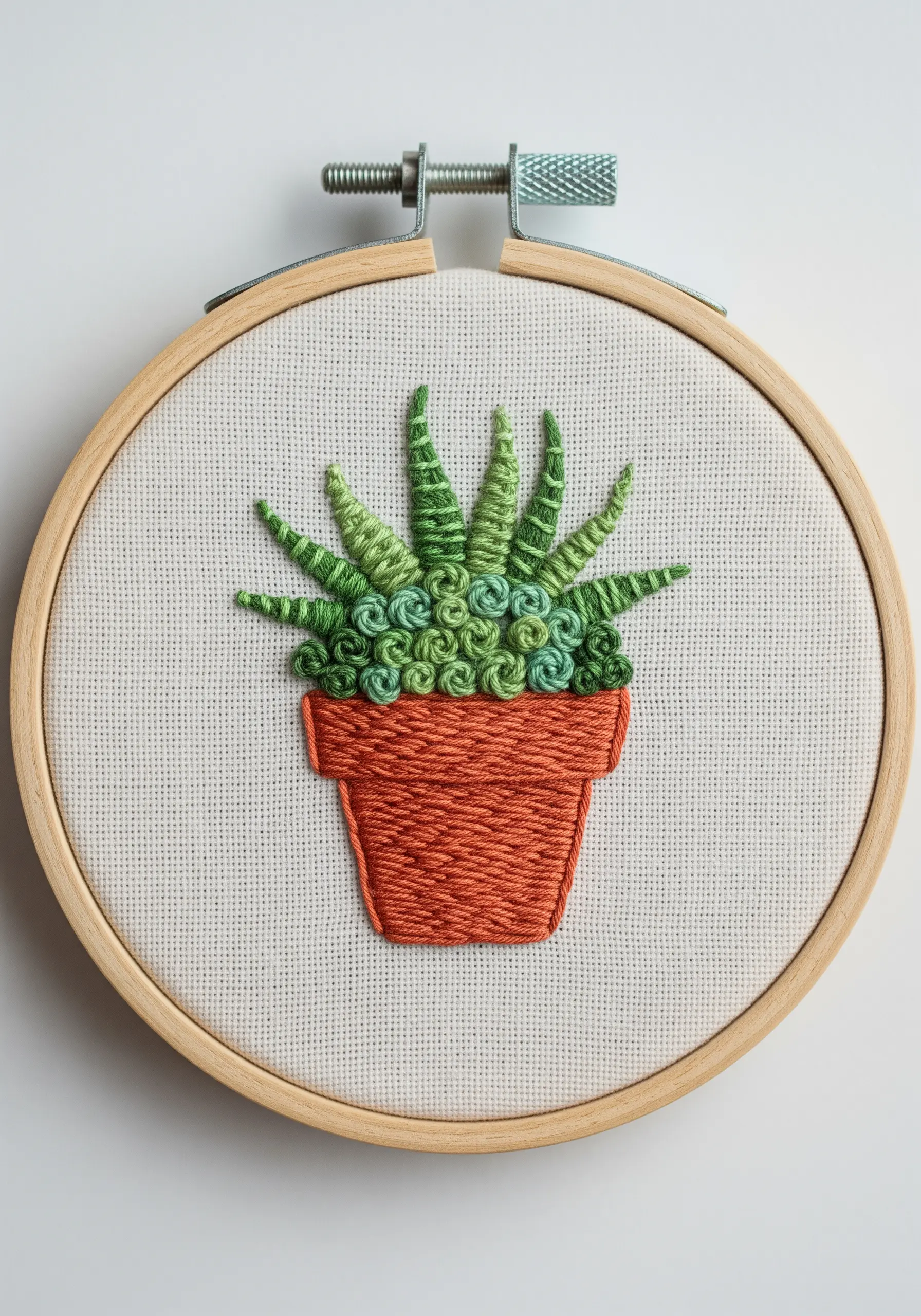 Embroidered succulent in a pot, using French knots, bullion stitches, and satin stitch.