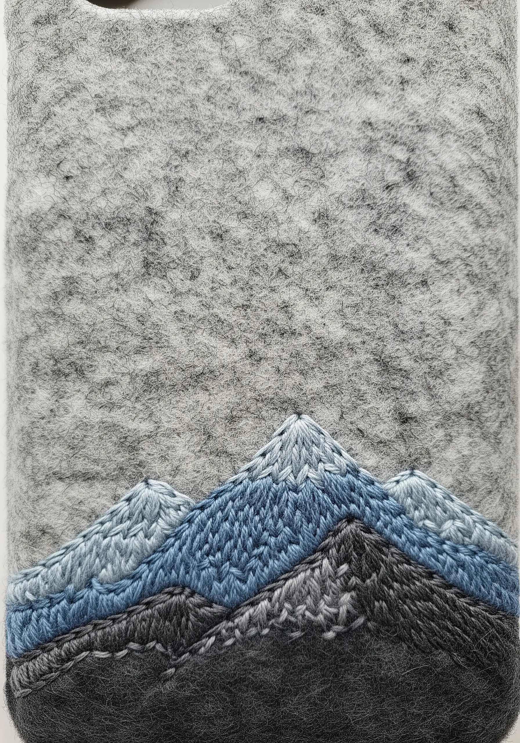A mountain range with thread-painted peaks in shades of blue and grey on a felted case.