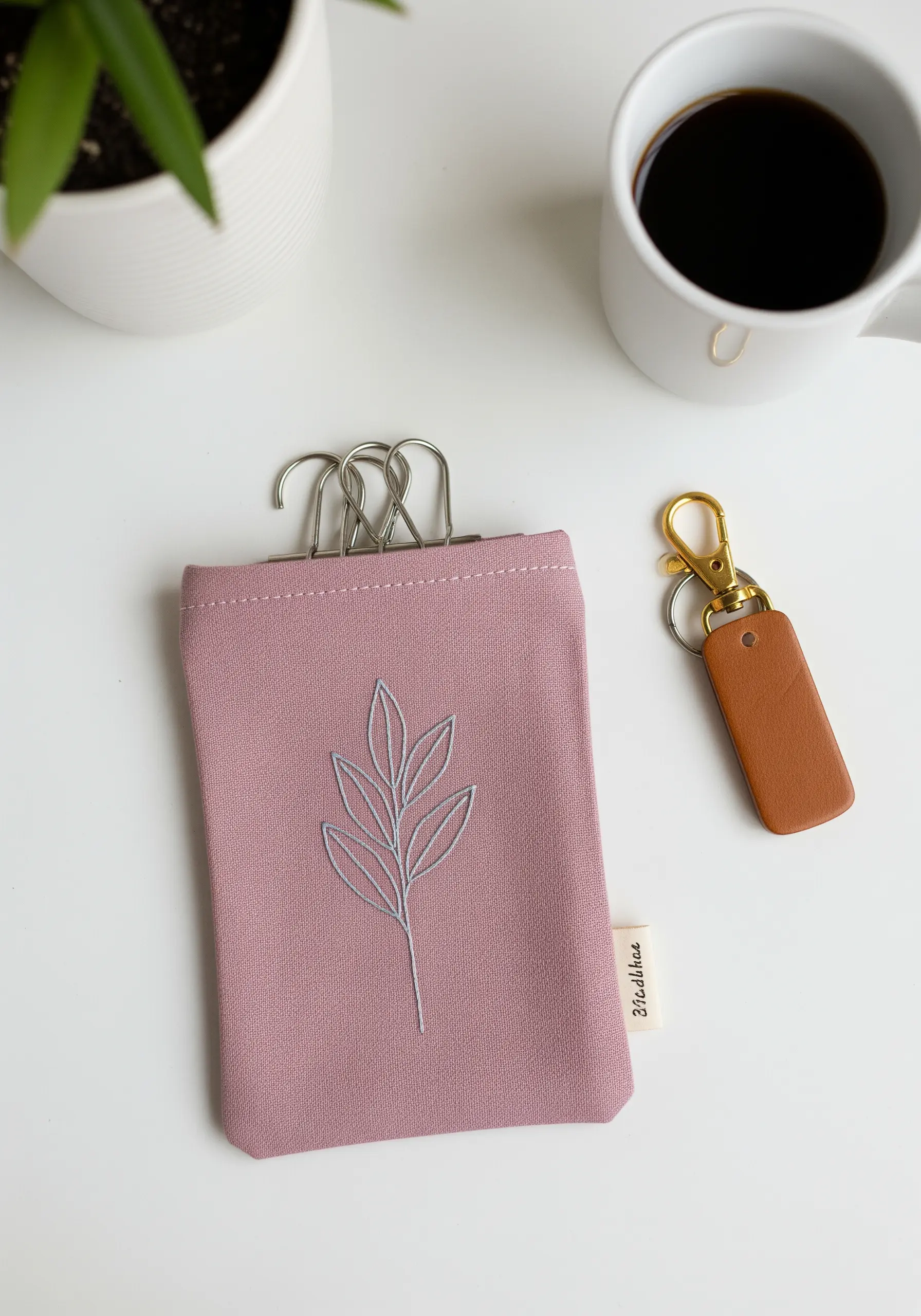 A simple leaf sprig embroidered in light grey on a dusty rose fabric pouch.