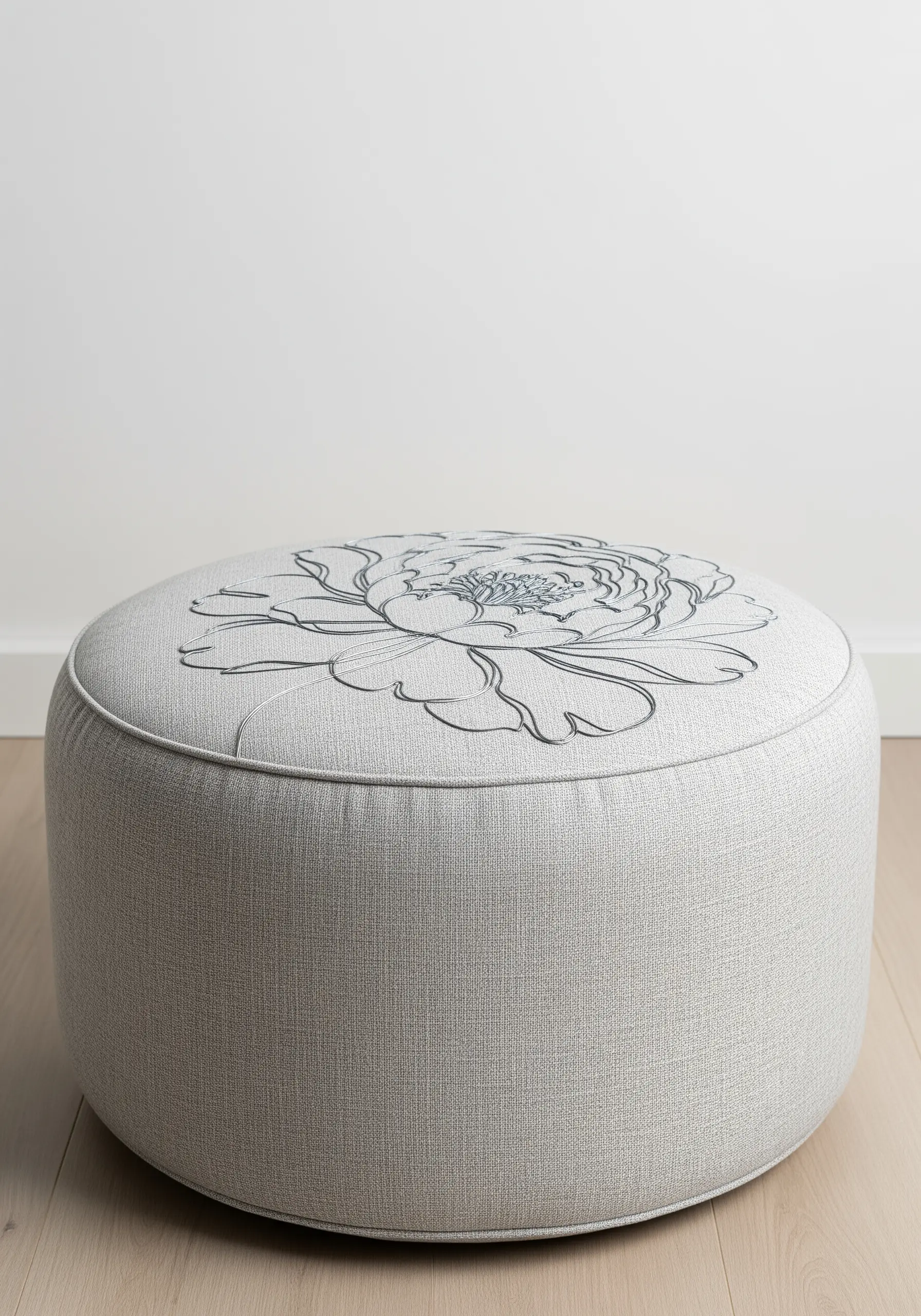 Large-scale one-line peony embroidered on the top of a round, upholstered ottoman.