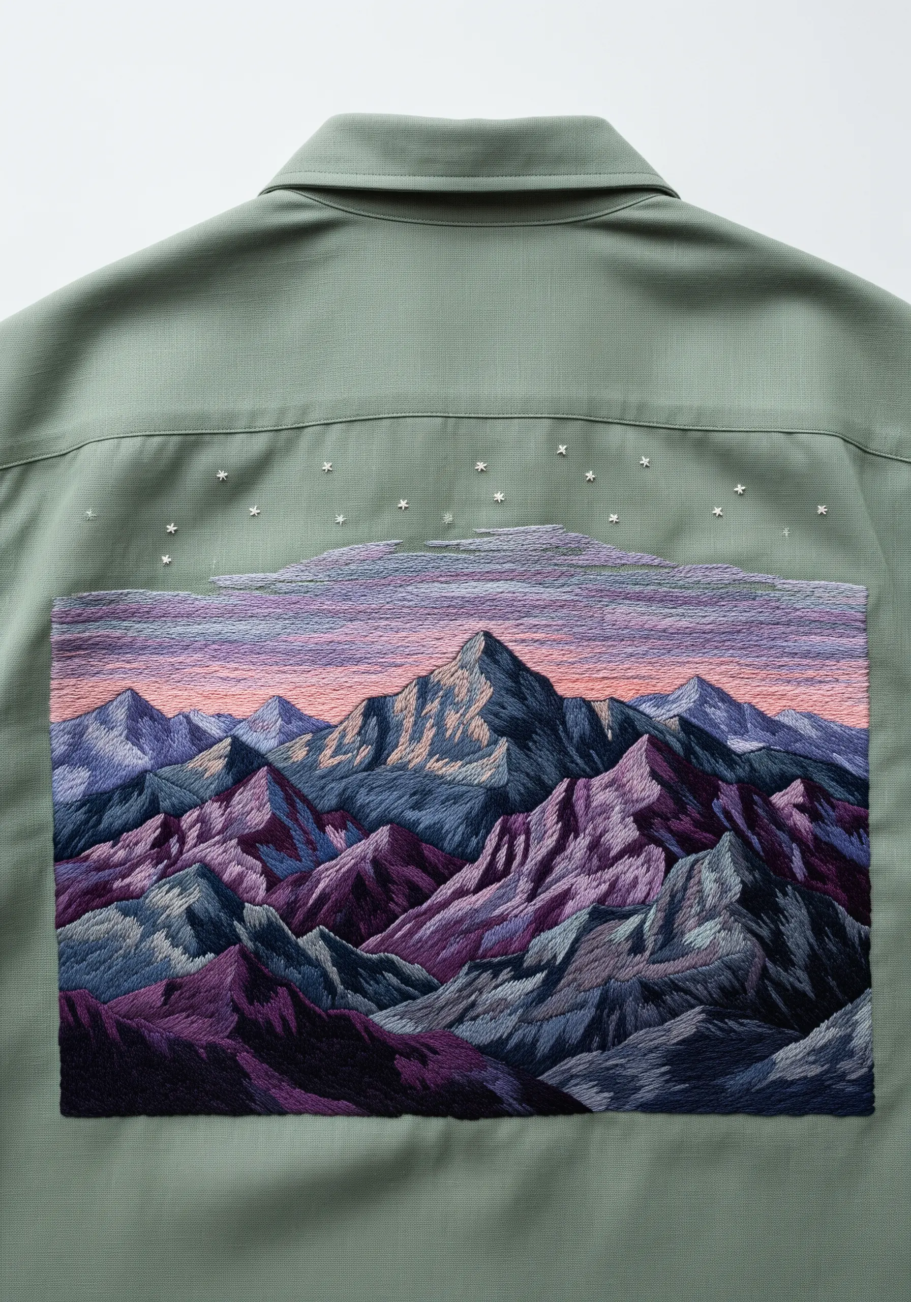 Embroidered mountain range at sunset with a pink and purple sky on a green shirt.