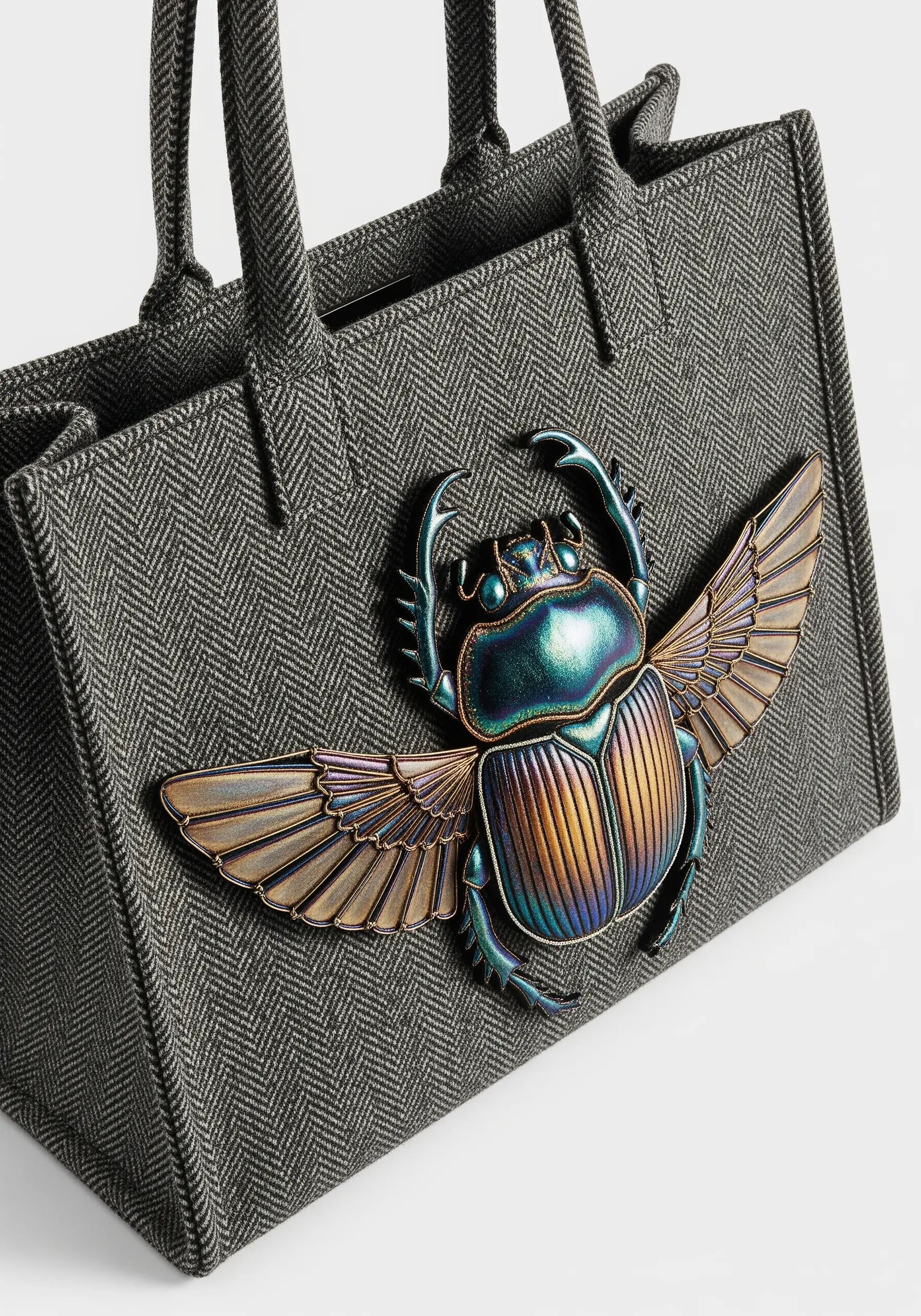 A 3D stumpwork scarab beetle with iridescent wings attached to a grey herringbone tote bag.