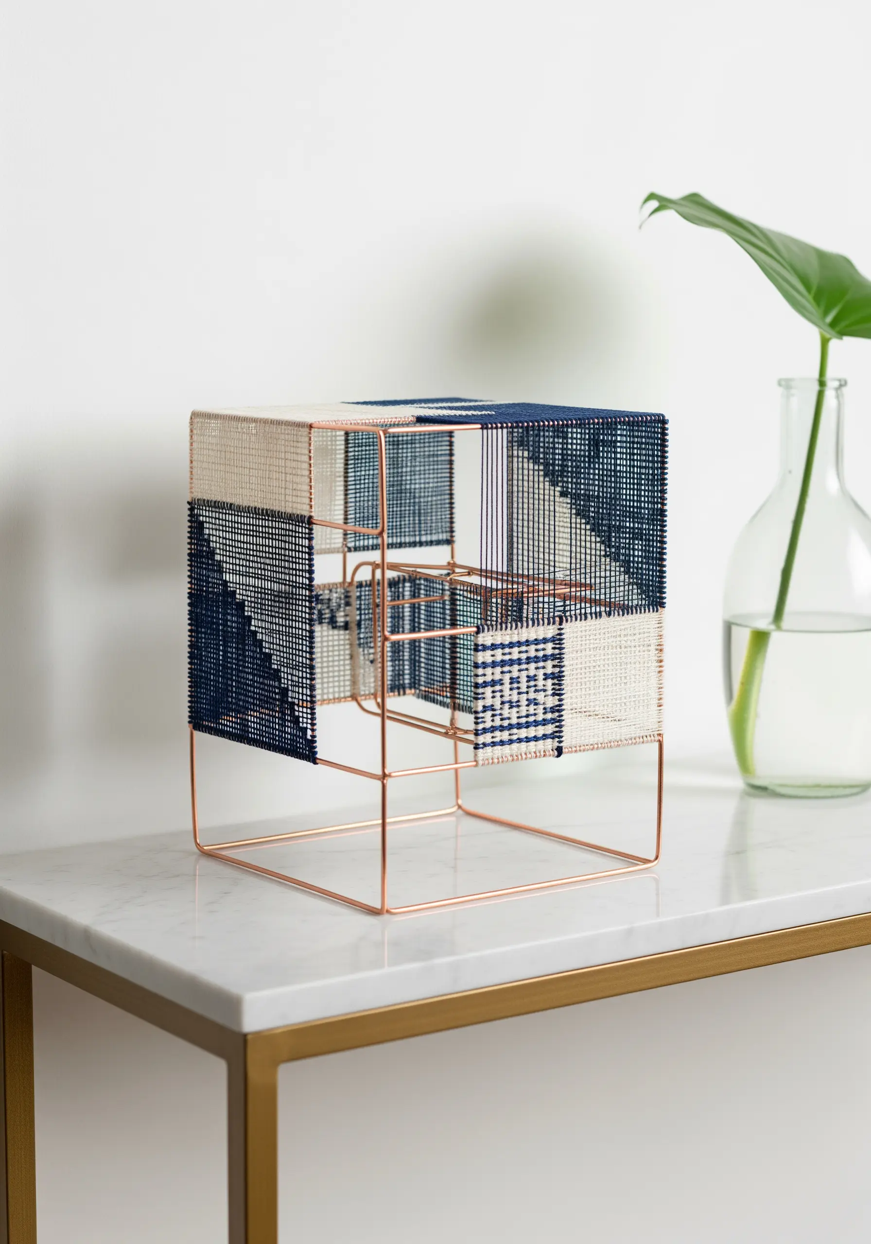 A cube-shaped sculpture made from woven blue and white threads on a thin copper frame.