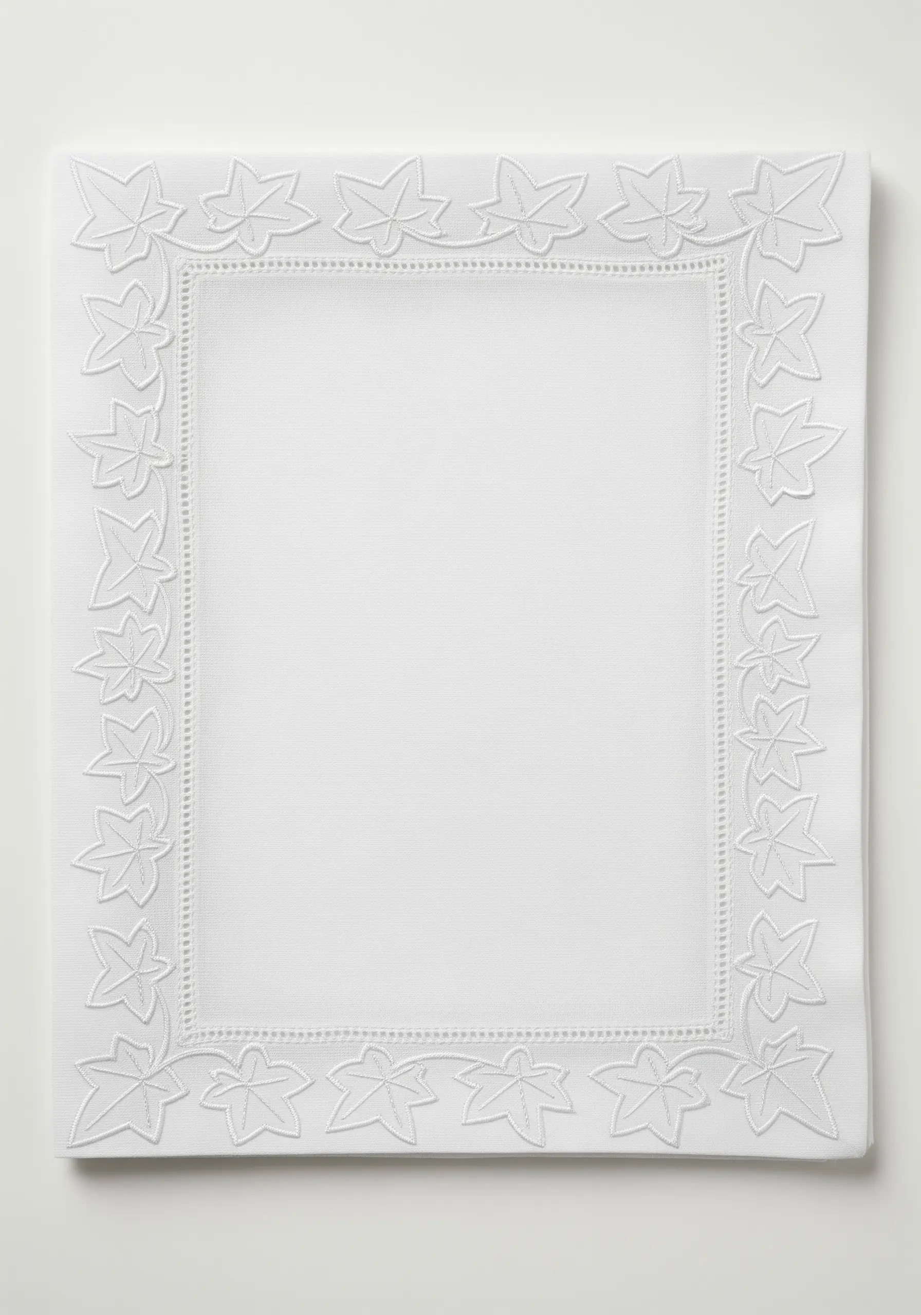 White-on-white ivy leaf border with raised satin stitch on a white linen napkin.