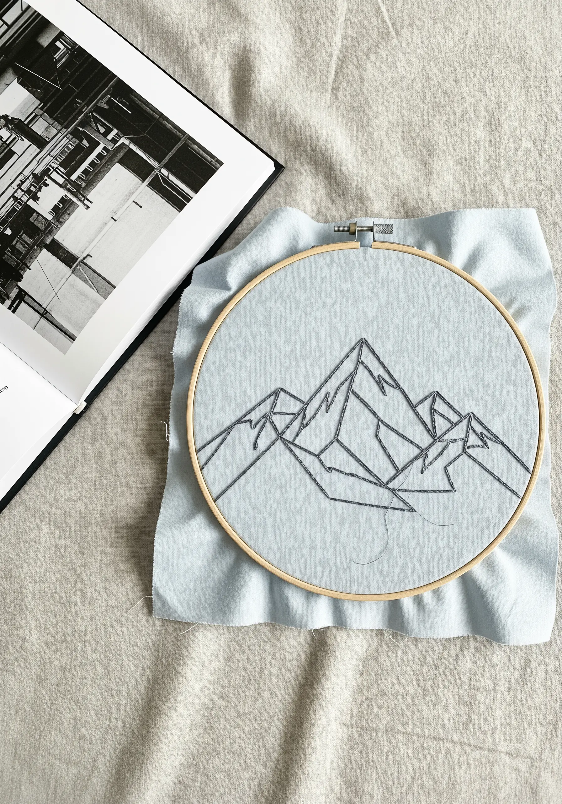 Minimalist line art embroidery of a mountain range on light blue fabric in a hoop.