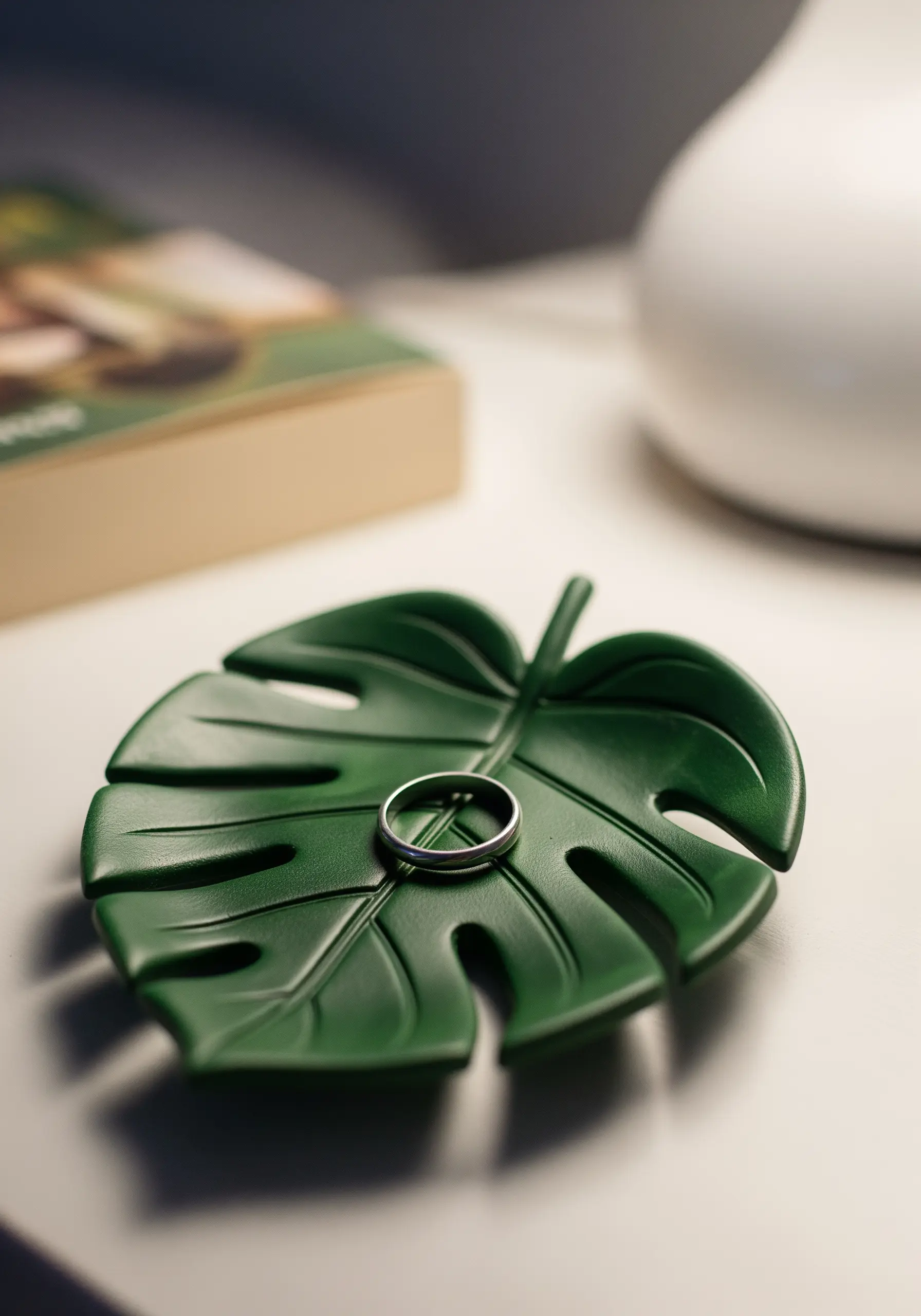 A green, monstera-leaf-shaped ceramic dish holding a silver ring on a white surface.