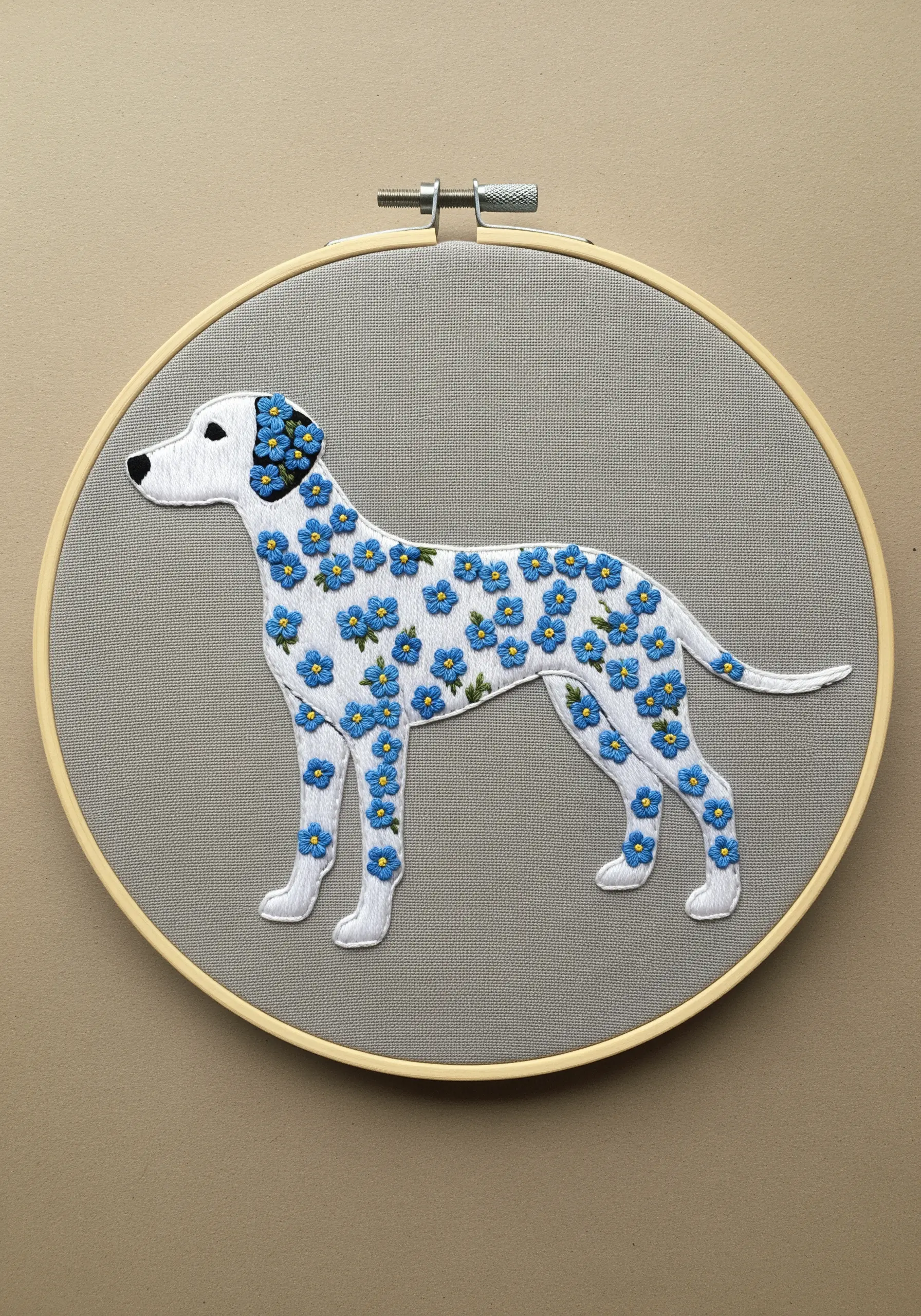 Stylized embroidery of a Dalmatian silhouette, where the spots are made of tiny blue flowers.