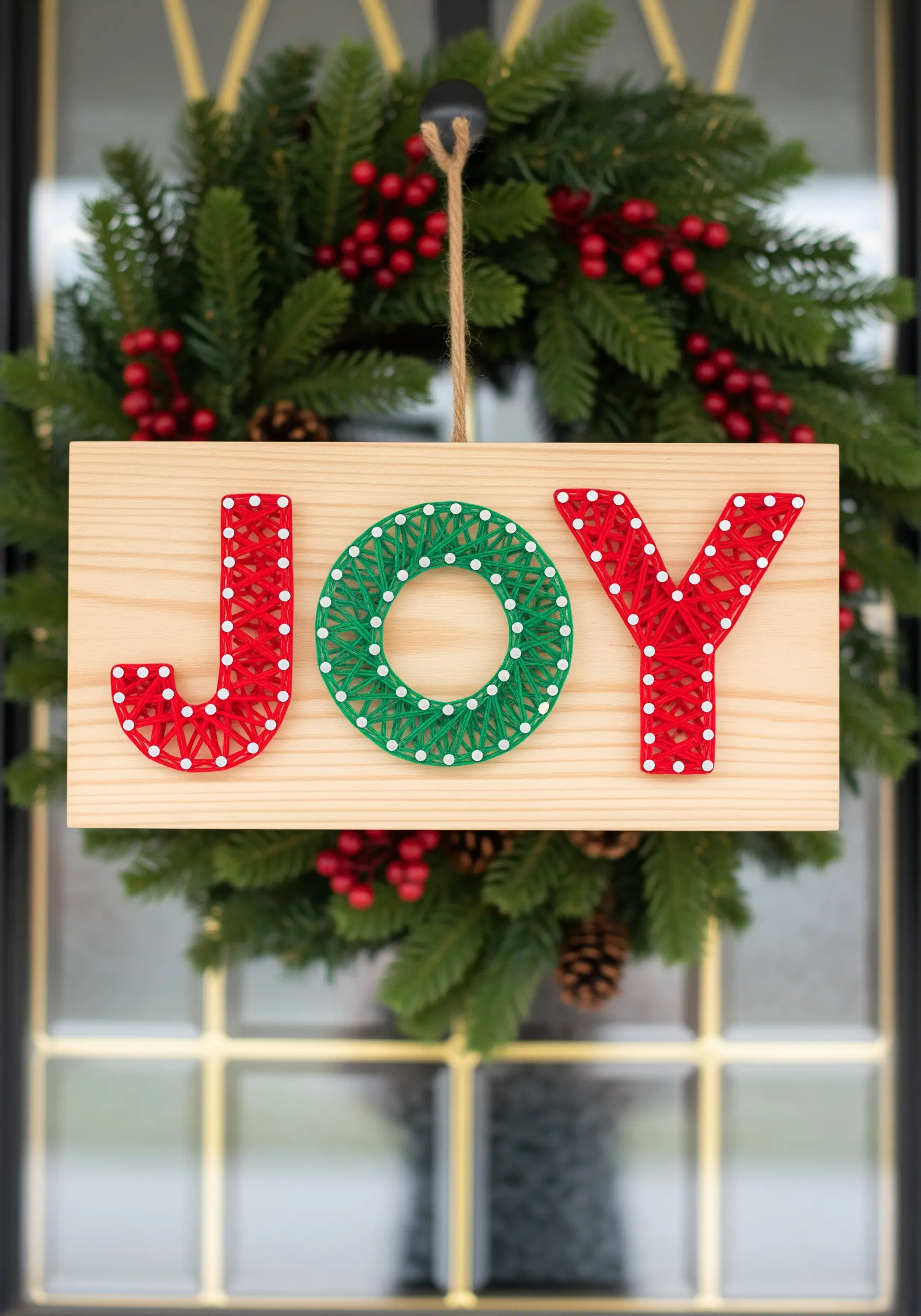 String art sign spelling 'JOY' in red and green thread on a wood board.