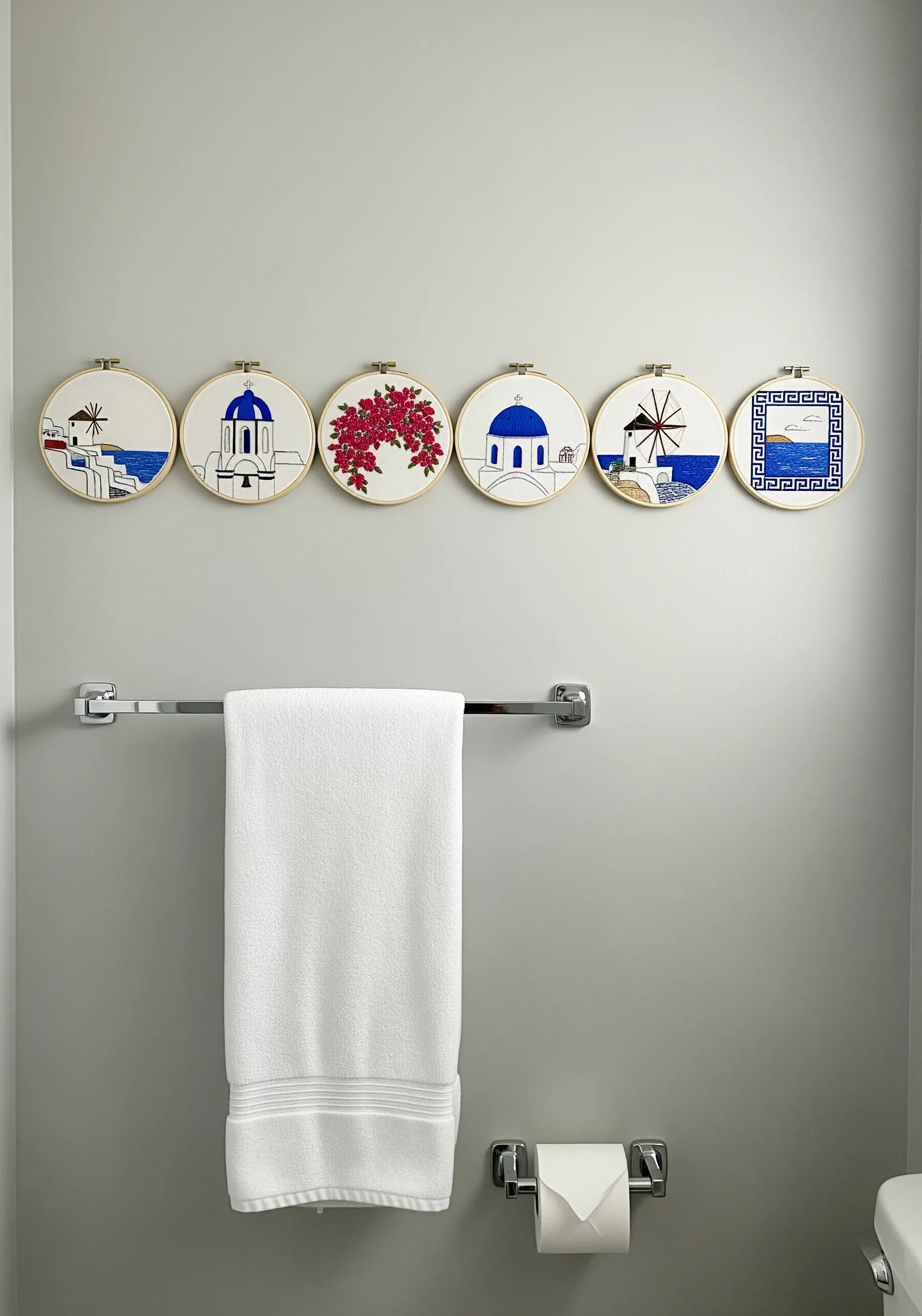Six Greece-themed embroidery hoops in blue and white arranged in a line above a towel rack.