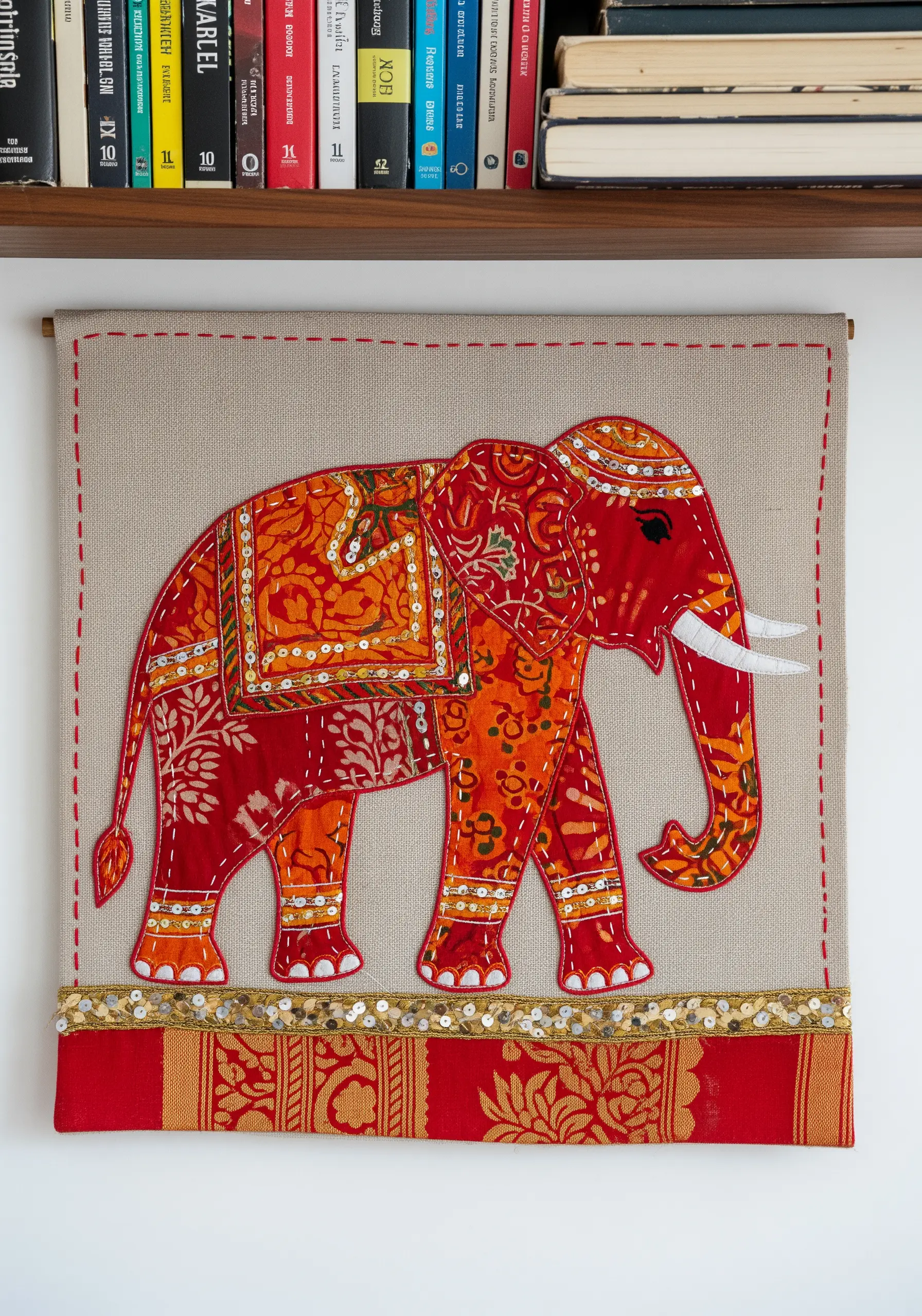 Appliqué elephant wall hanging made from red and orange patterned fabrics with sequin details.