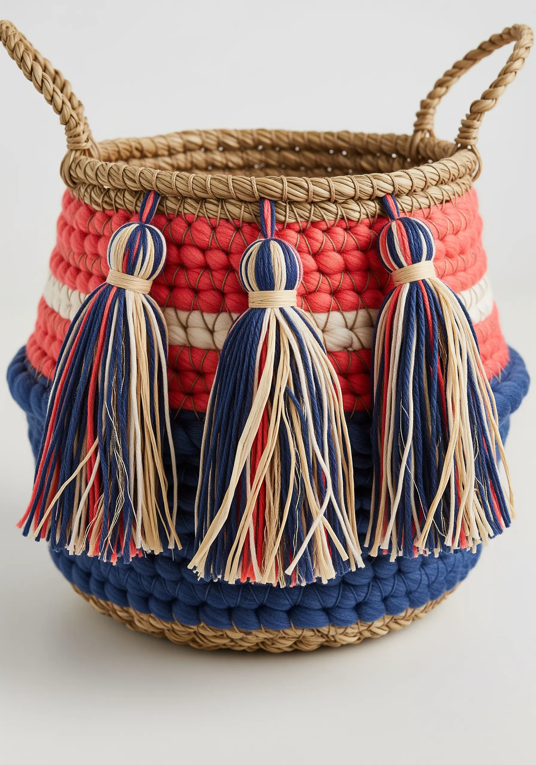 A woven seagrass basket decorated with red and blue yarn wrapping and multi-colored tassels.