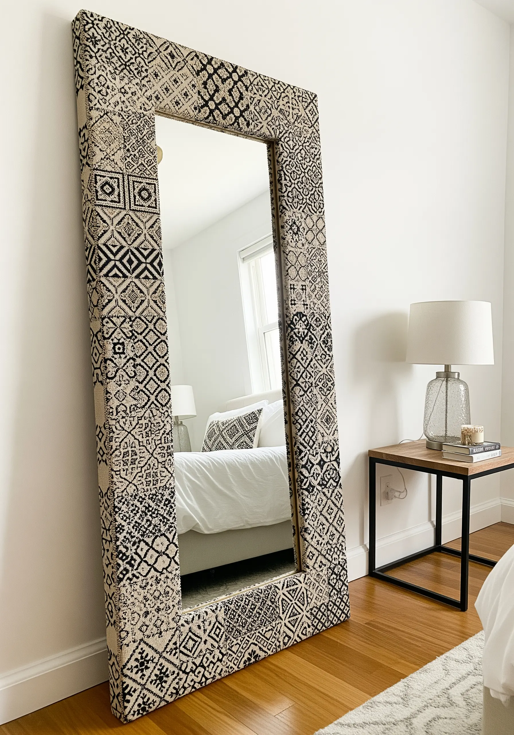 A large floor mirror with its frame covered in a black and beige geometric patterned fabric.