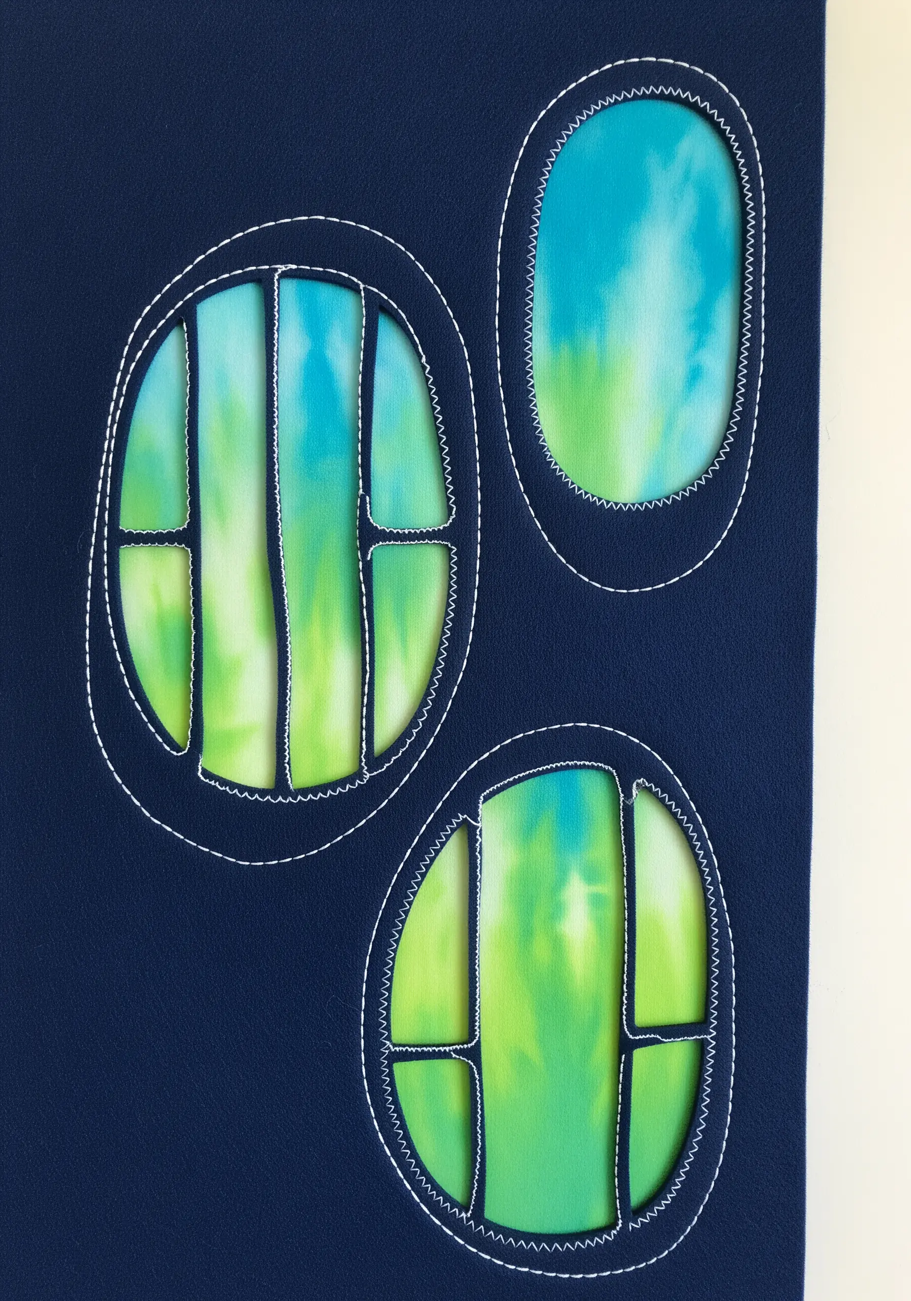A dark blue fabric with oval cut-outs revealing a tie-dyed green and blue fabric underneath.