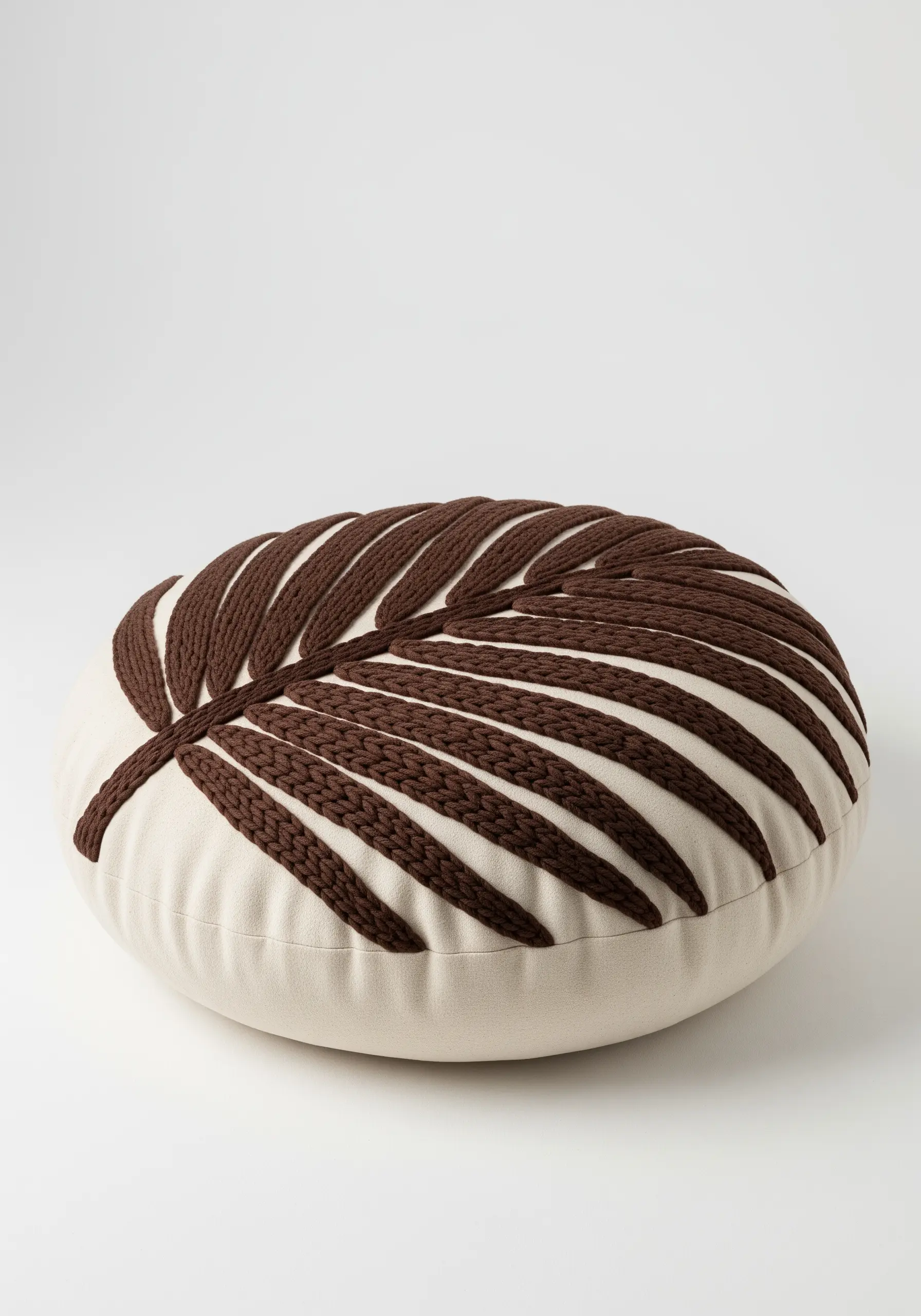 A round floor cushion with a bold palm leaf embroidered using thick, chunky brown yarn.