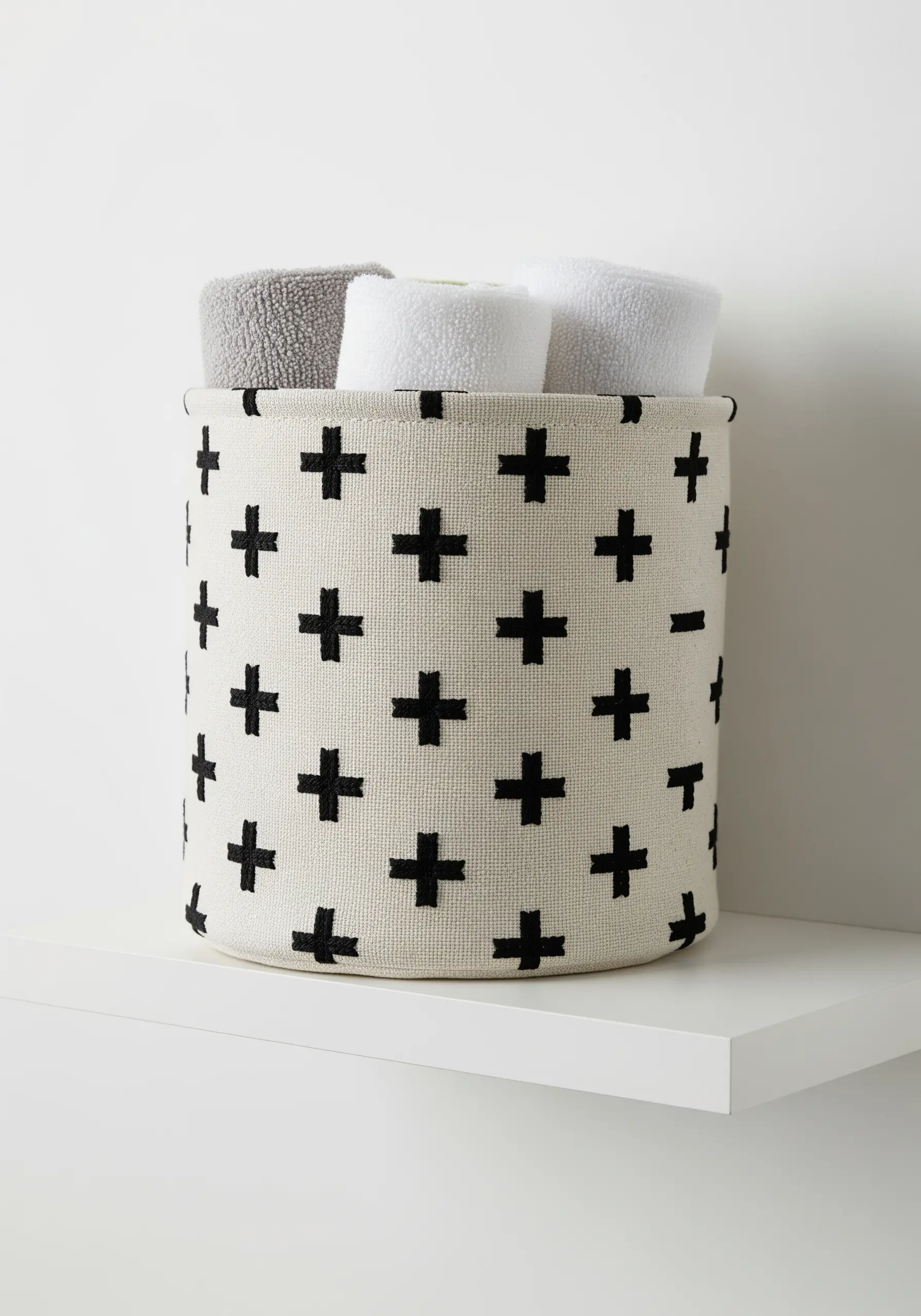A cylindrical off-white fabric basket decorated with a repeating black Swiss cross pattern.