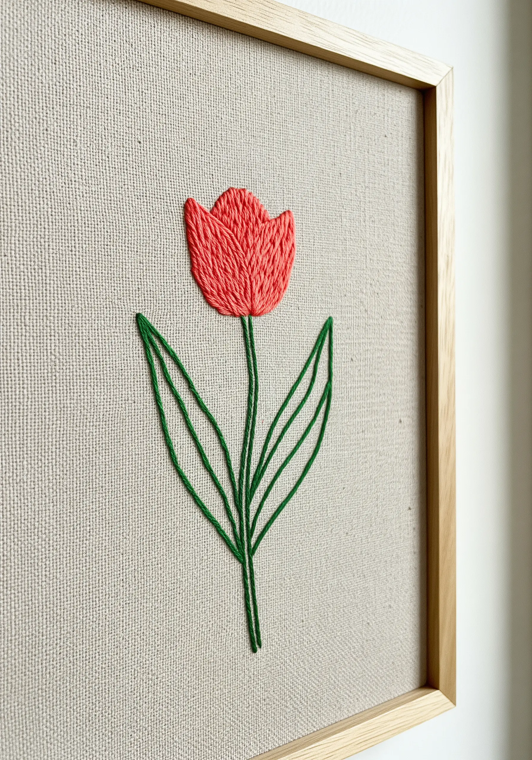 A simple embroidered tulip with coral satin-stitched petals and green stem.