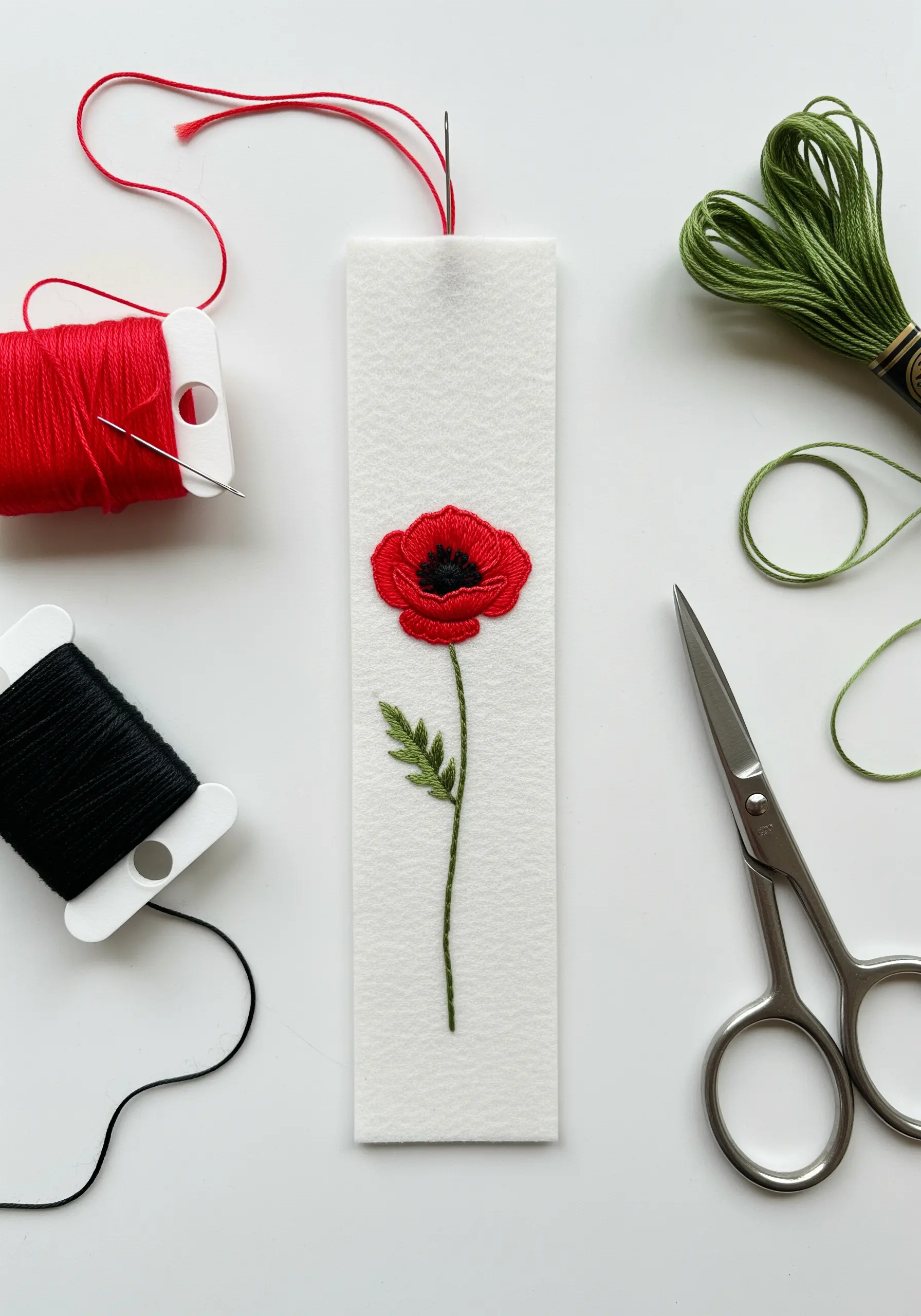A single red poppy with a black center stitched onto a white felt bookmark.