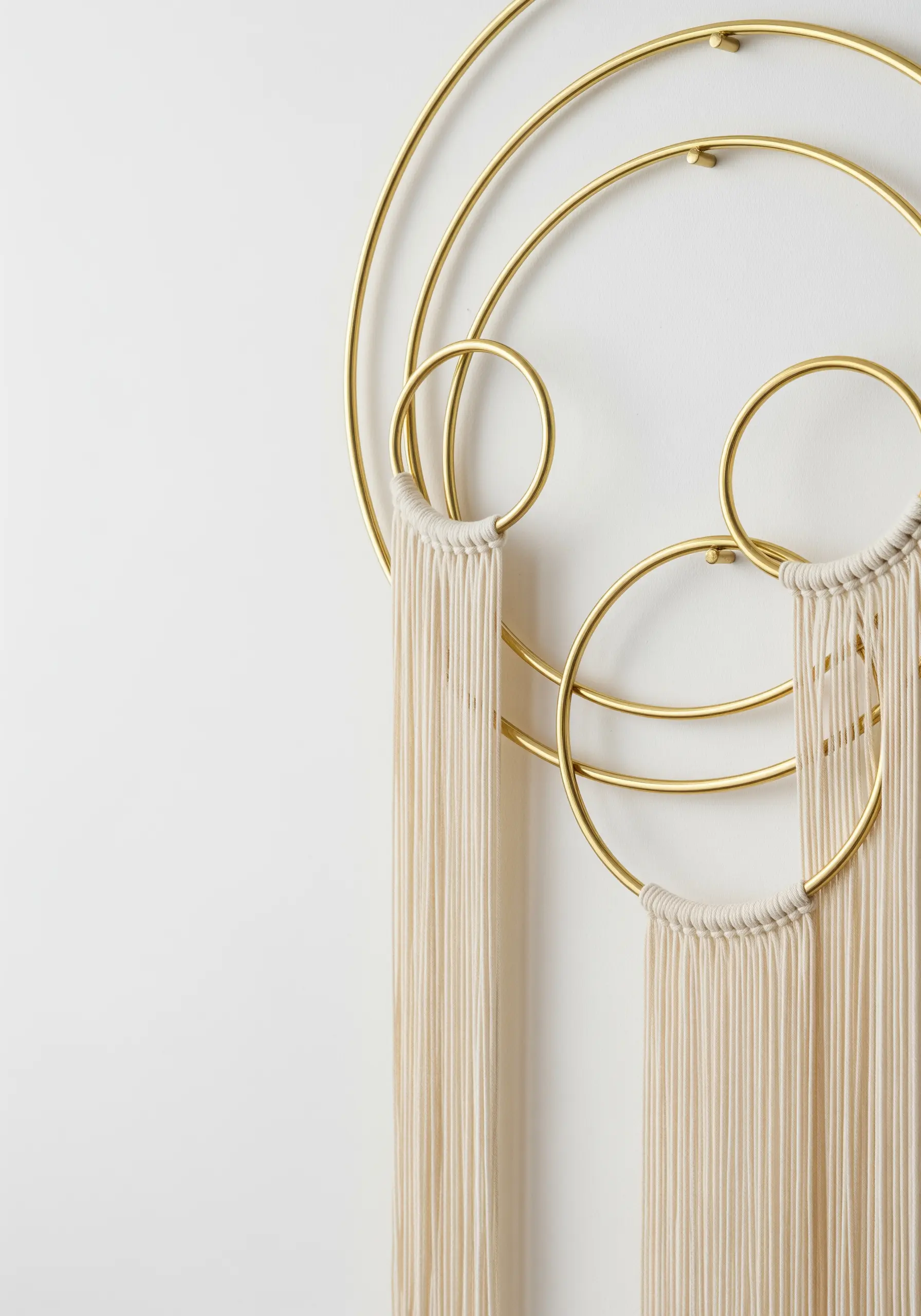 A modern wall hanging with cream yarn descending from a series of interlocking brass hoops.