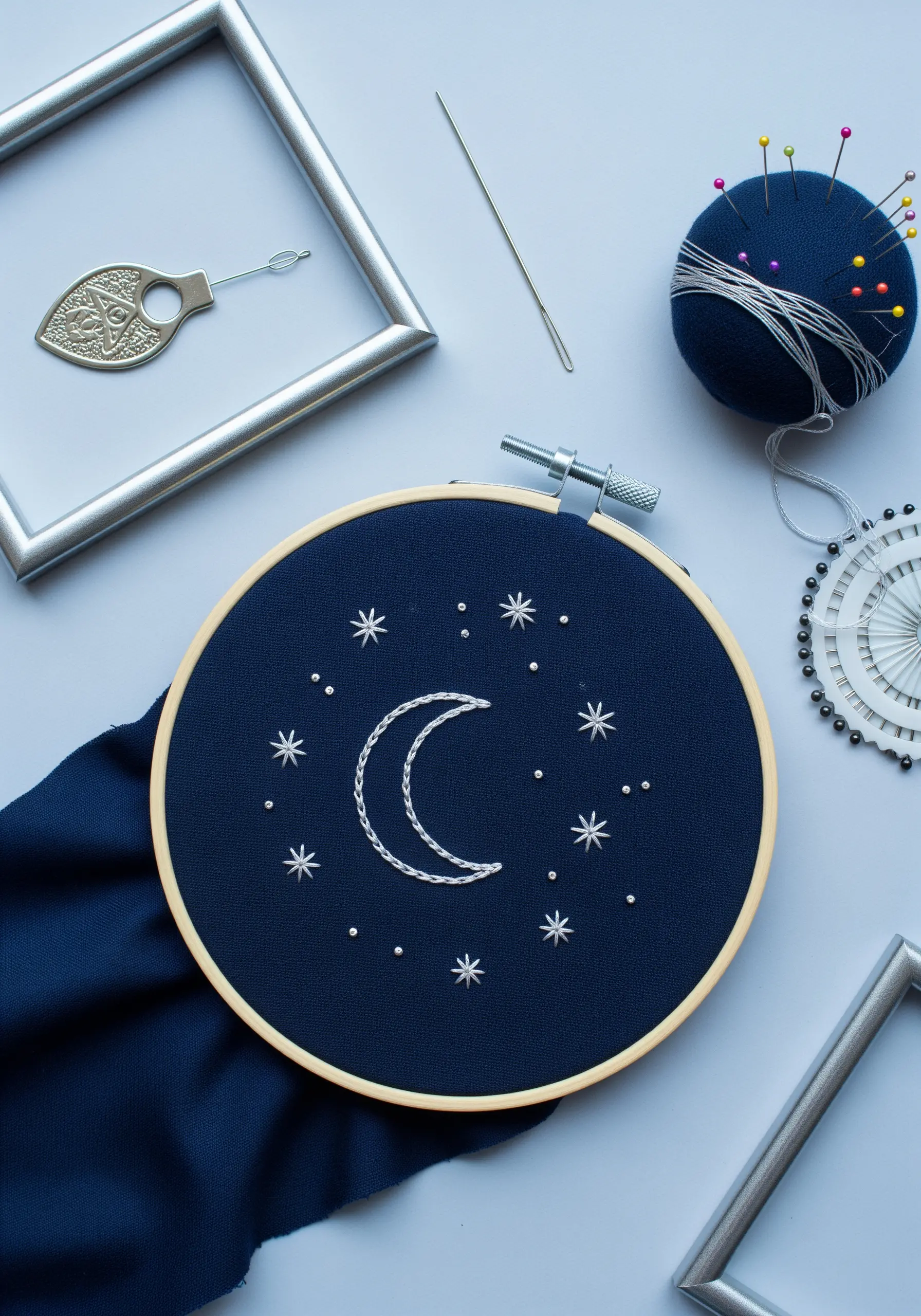 A crescent moon and stars embroidered with white thread on dark navy fabric.